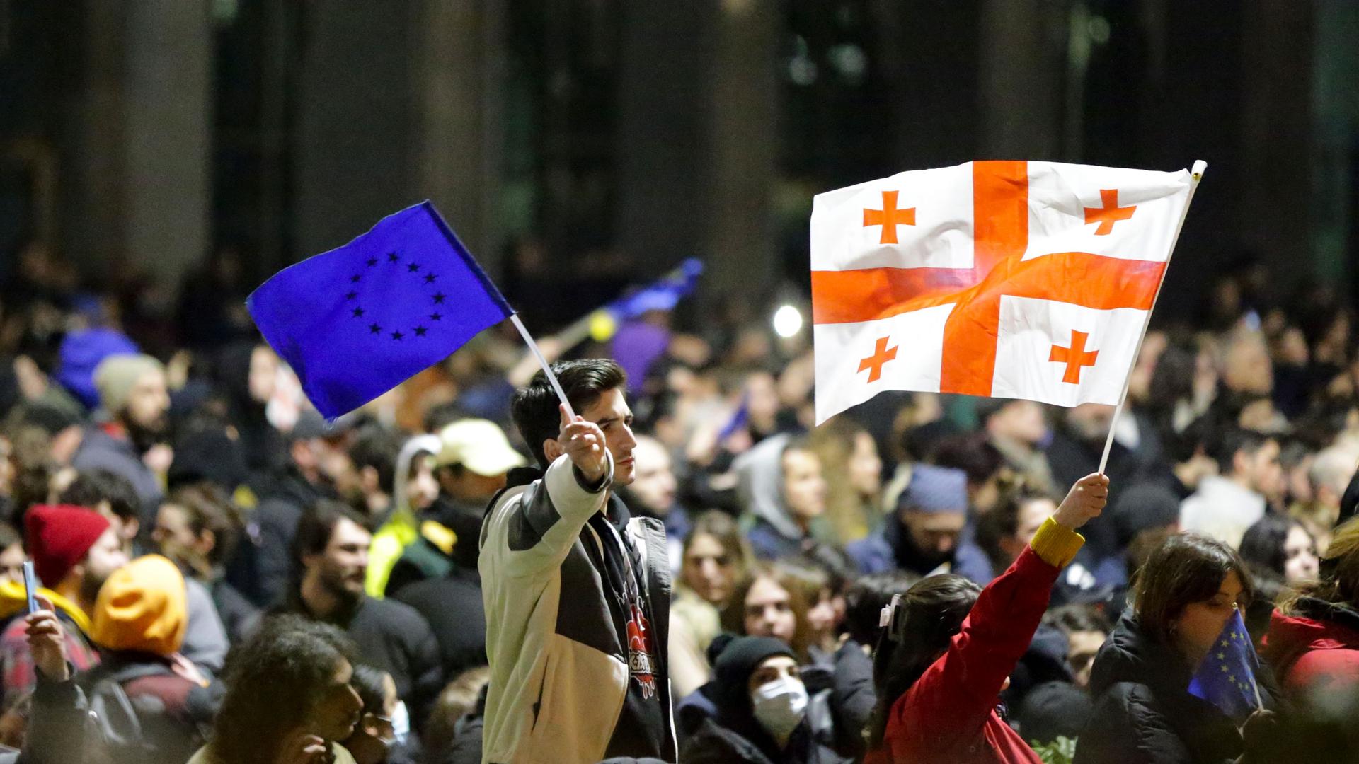 Protesters wave a Georgian national and EU flags as they rally against a draft law 
