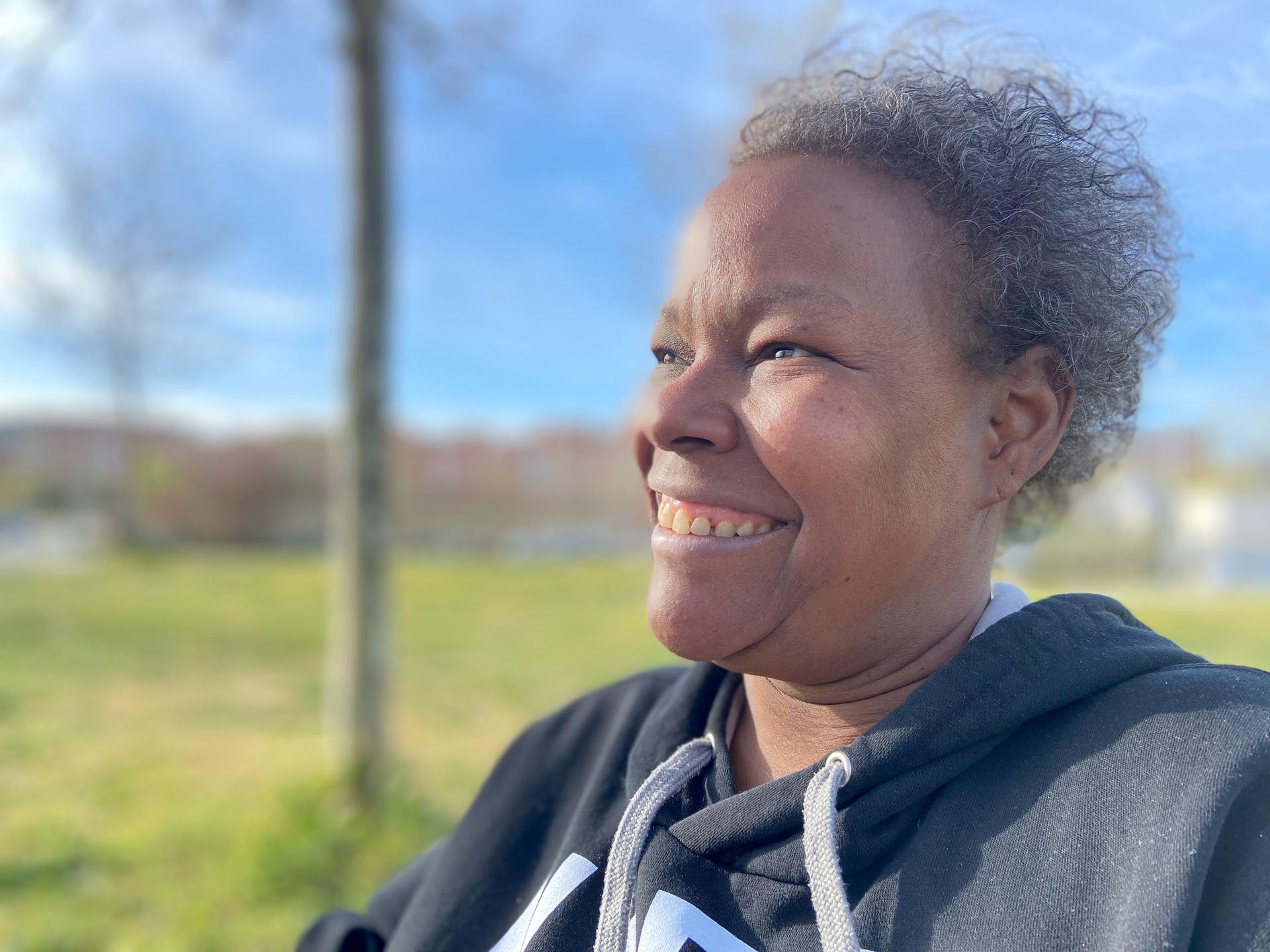 Vicky sits in a park in Madrid. She’s smiling because her hospice caretakers have arranged for her to fly home to the Dominican Republic to visit her mom and family one last time.