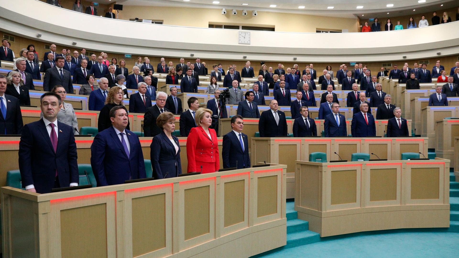 In this photo provided by The Federation Council of The Federal Assembly of The Russian Federation Press Service, lawmakers of Federation Council of the Federal Assembly of the Russian Federation listen to the national anthem at a session in Moscow, Russi