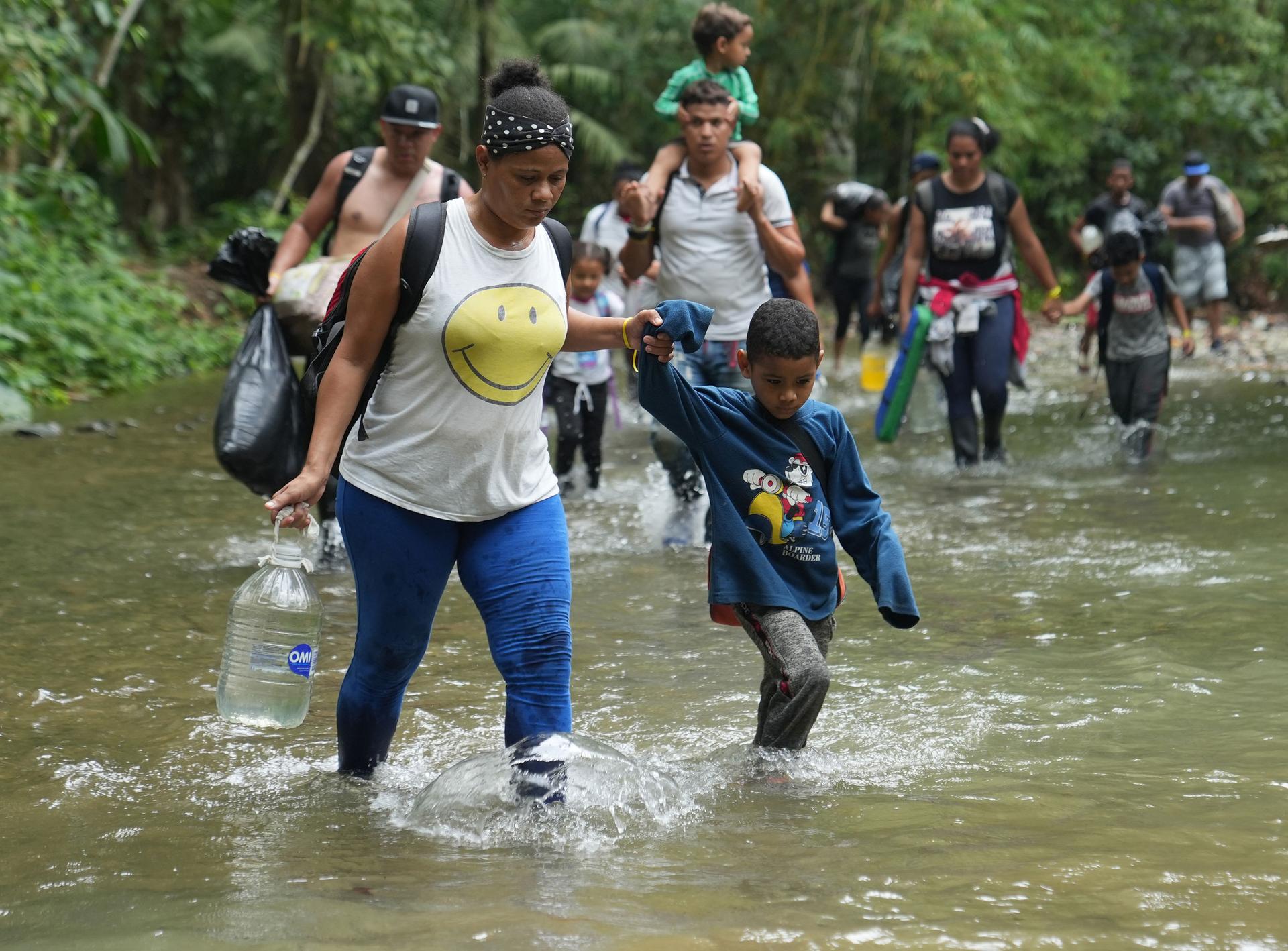 A Venezuelan migrant travels with her child and crosses a stream, as they start the trek across the Darien Gap.