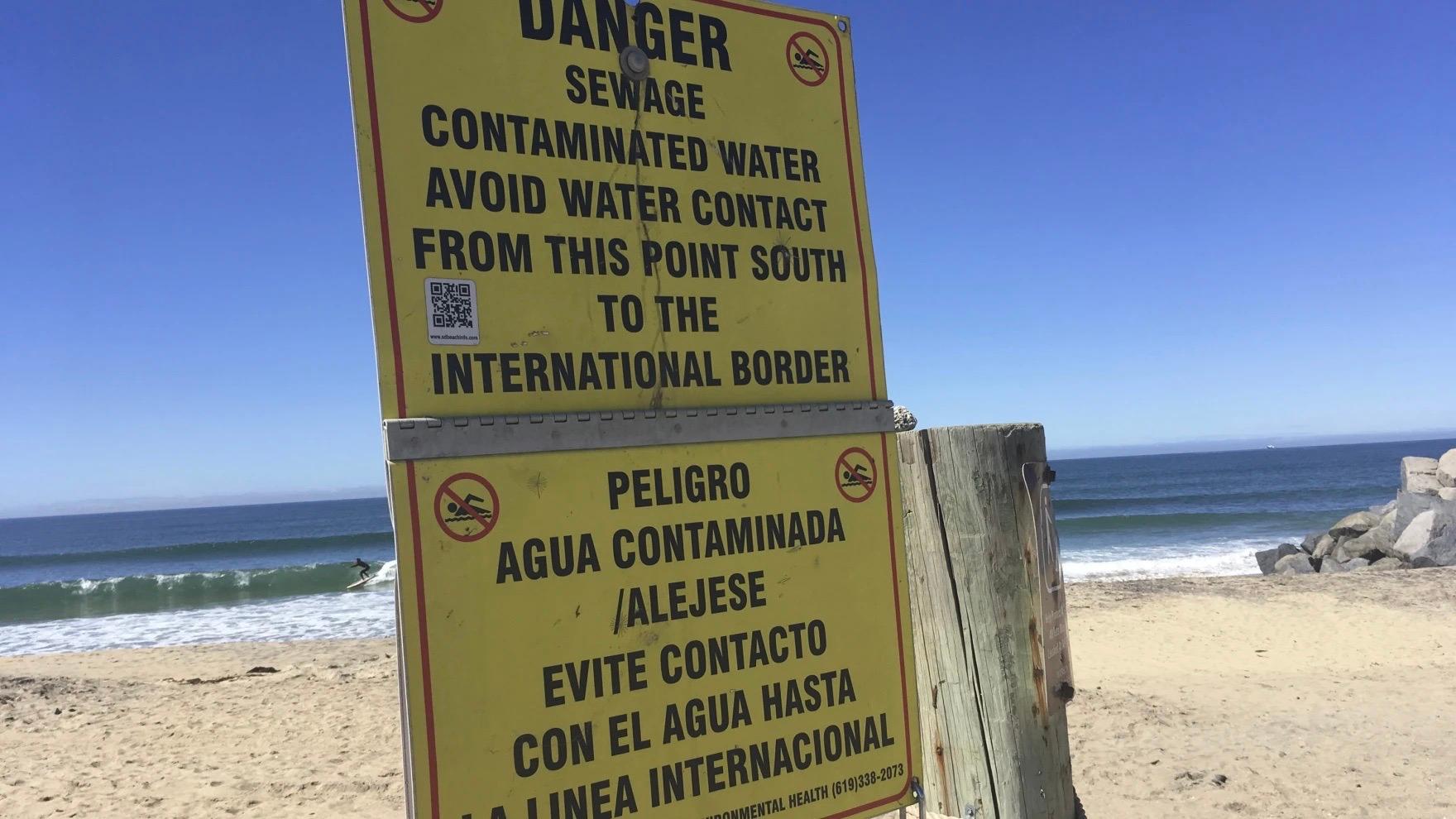 Yellow sign on beach warning people to stay out of water because of pollutants, in Tijuana River Valley