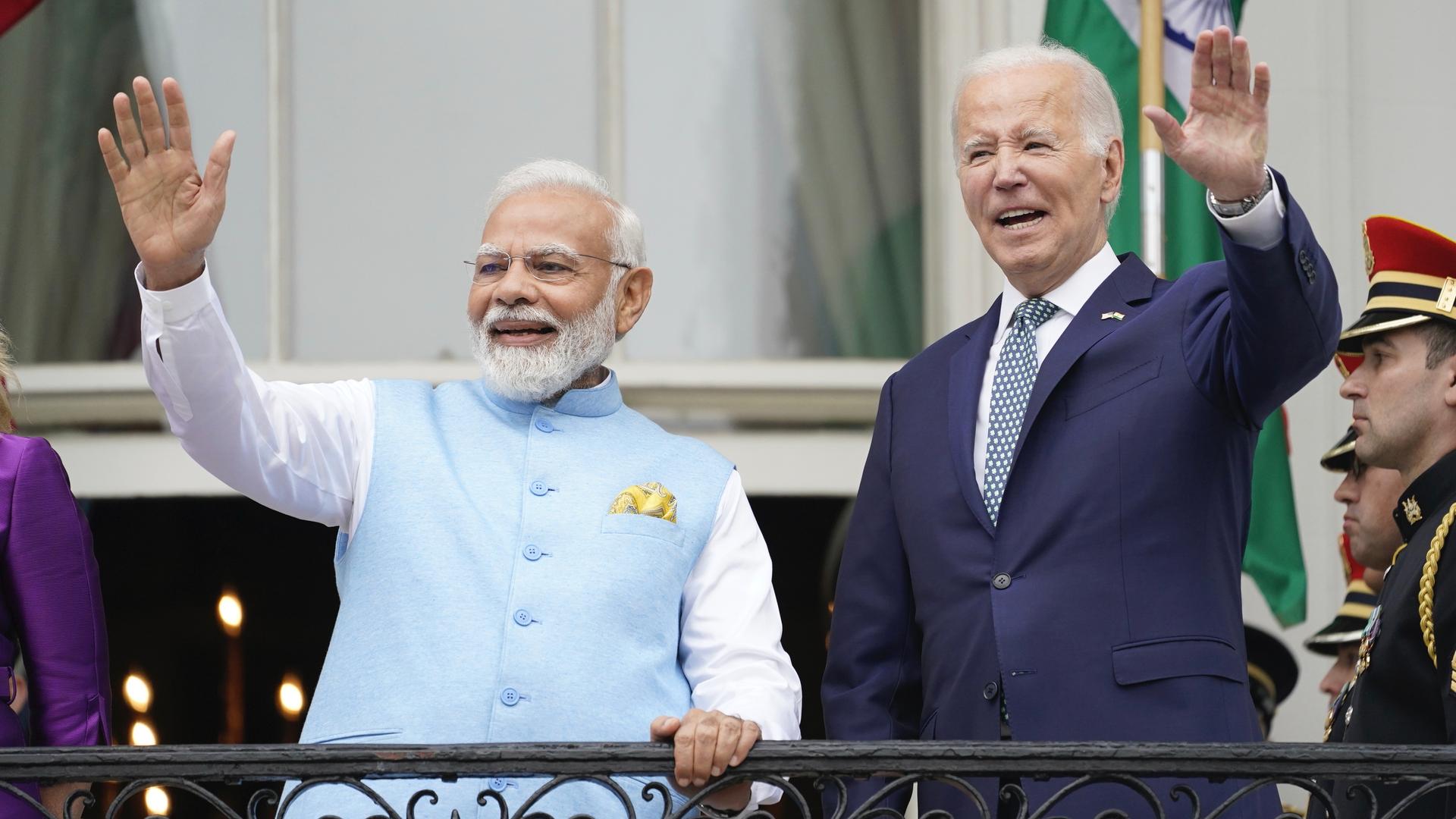 Two men, US President Biden and Indian Prime Minister Narendra Modi standing with the arms stretched outward to wave