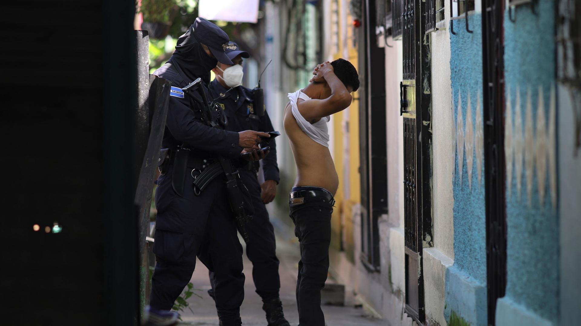 A police officer searches and checks the documents of a man living in the Kiwanis Community, during a preventive patrol in search of gang members in Soyapango, El Salvador, Aug. 16, 2022, amid a state of exception.