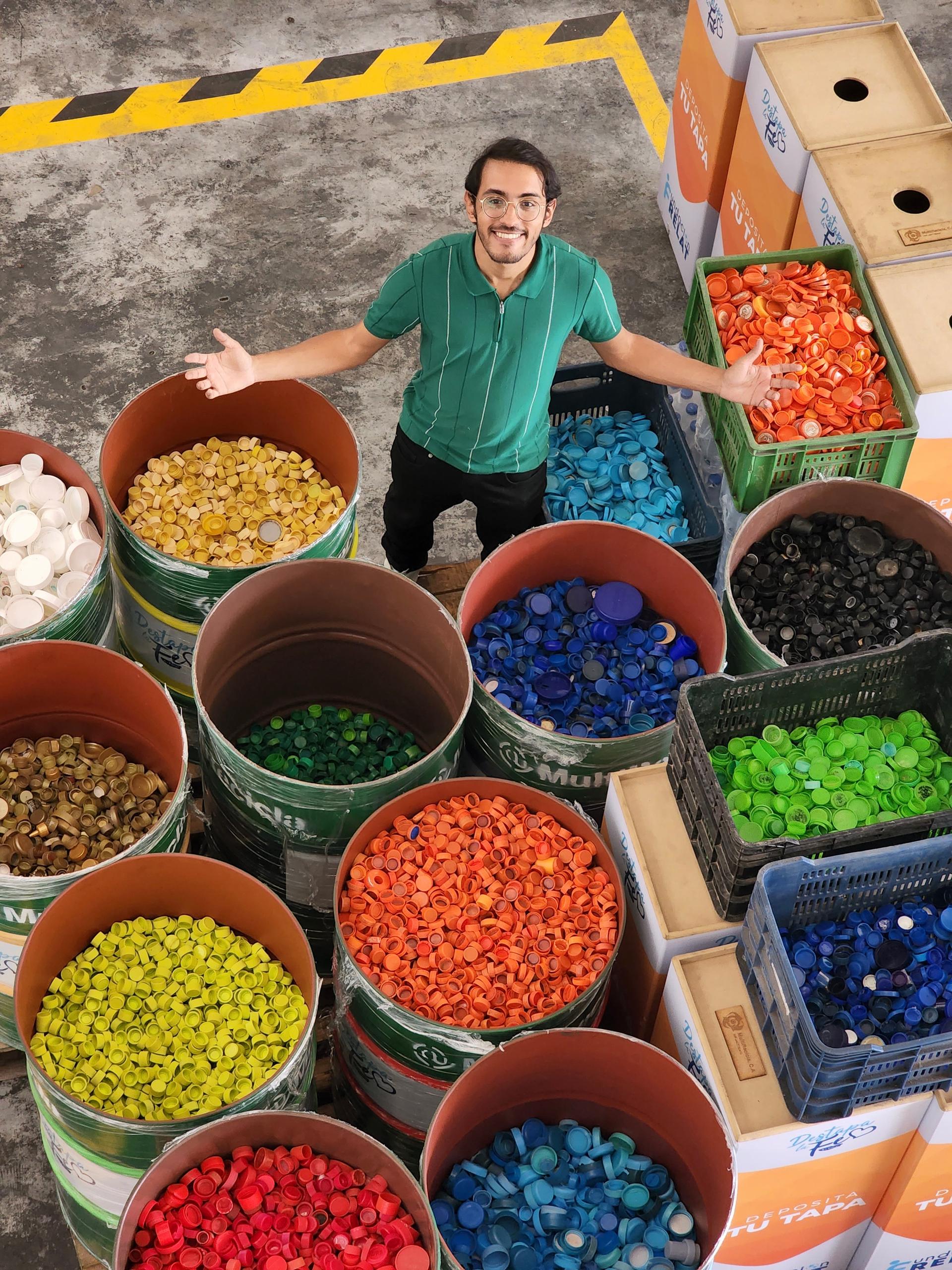 A man in a green shirt standing by bins of bottle caps separated by color
