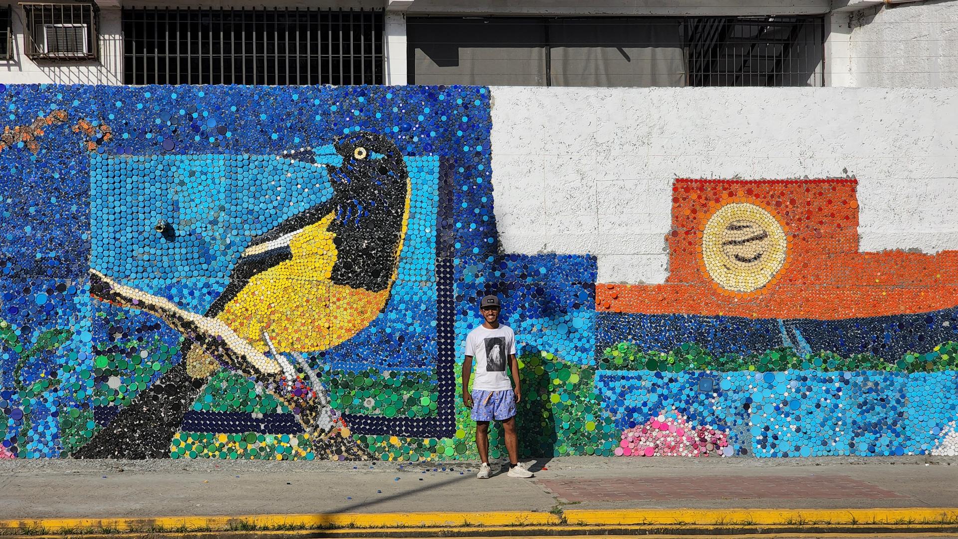 a man standing in front of a colorful bottle cap mural
