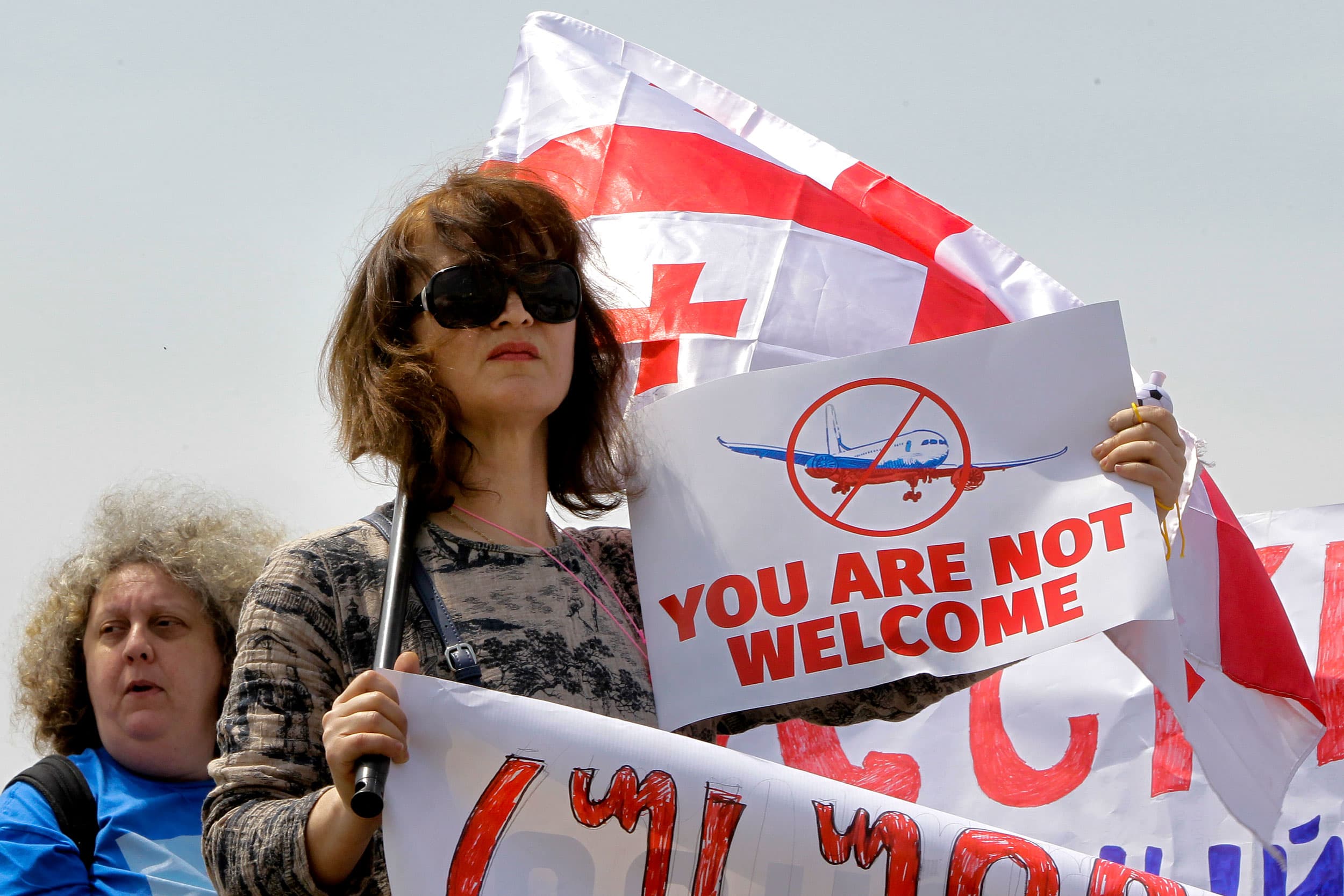 A Georgian opposition activist with a Georgian national flag attends a protest against the resumption of air links with Russia standing behind a police line at the International Airport outside Tbilisi, Georgia, Friday, May 19, 2023.