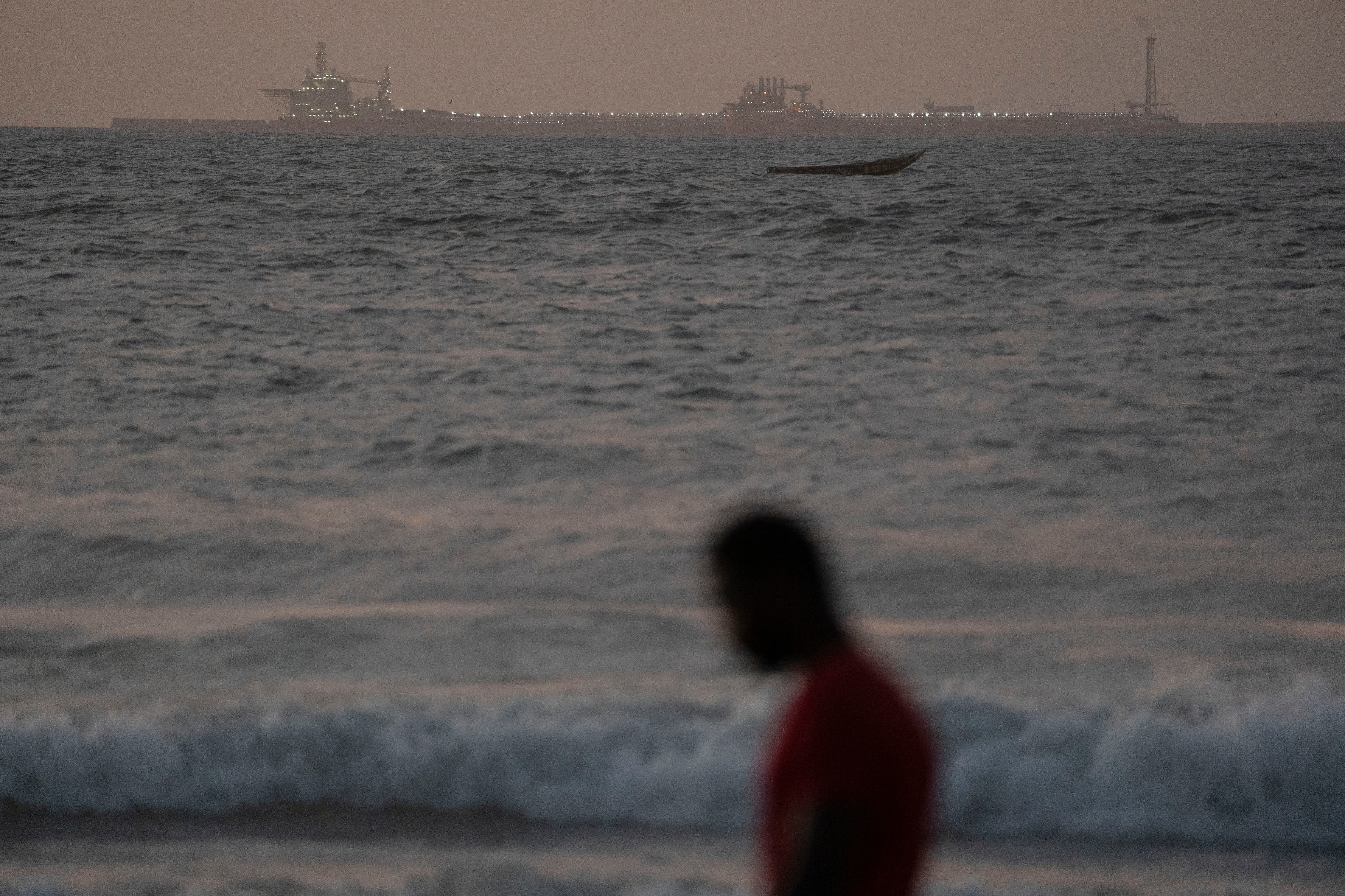 A man walks on the beach past an offshore gas terminal in Saint-Louis, Senegal, Jan. 19, 2023.