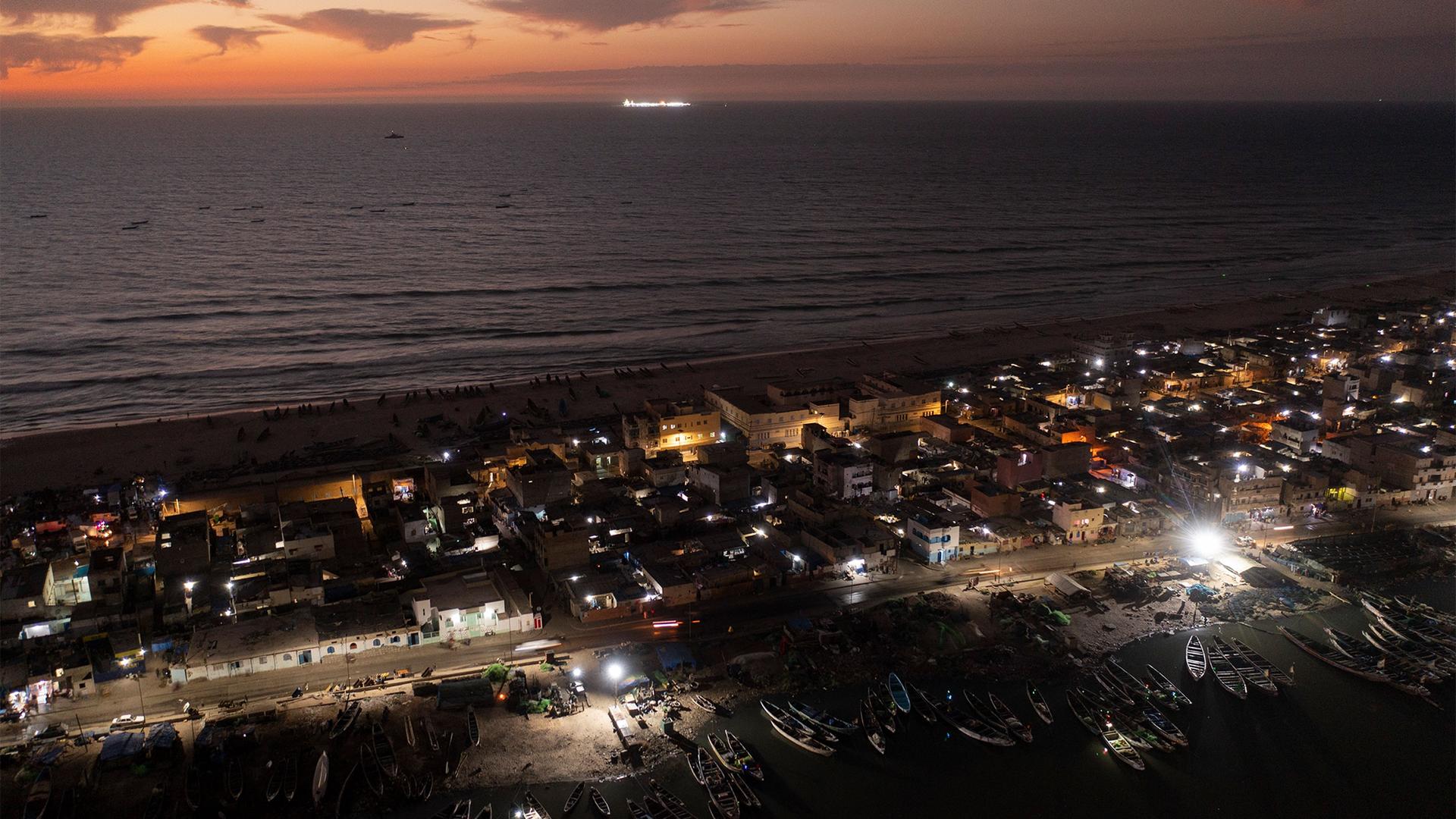 An offshore gas terminal is lit up amid the Atlantic Ocean as houses lay on the beachfront between the sea and the Senegal River, bottom, in Saint-Louis, Senegal, Jan. 18, 2023.