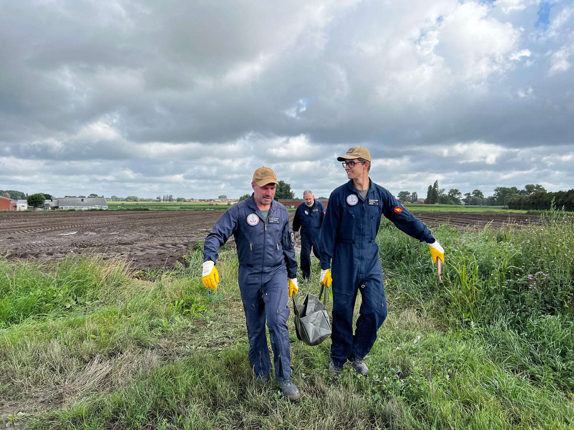 Members of Belgium’s bomb disposal unit Warrant Officer Steven de Meulenaere, left, and First Sergeant Sander Poelmans, right, carry a German 15-centimeter high explosive shell manufactured in 1914 away from the field where a farmer found it.