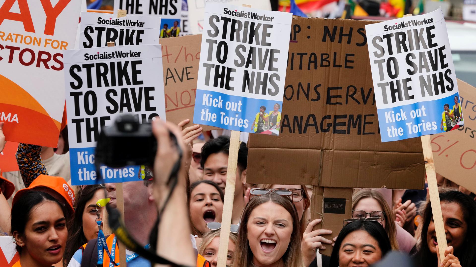 crowd of people holding signs with commentary about Britain's NHS