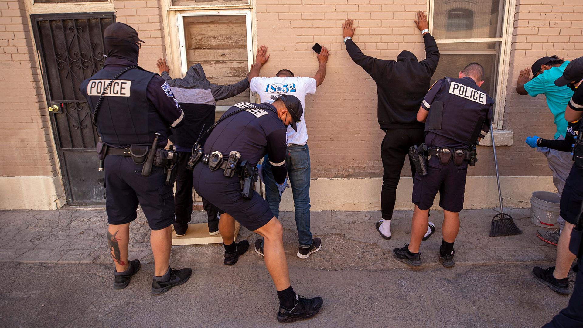 Under the suspicion of drug consumption, police officers frisk a group of migrants at a camp on a street in downtown El Paso, Texas, April 30, 2023.
