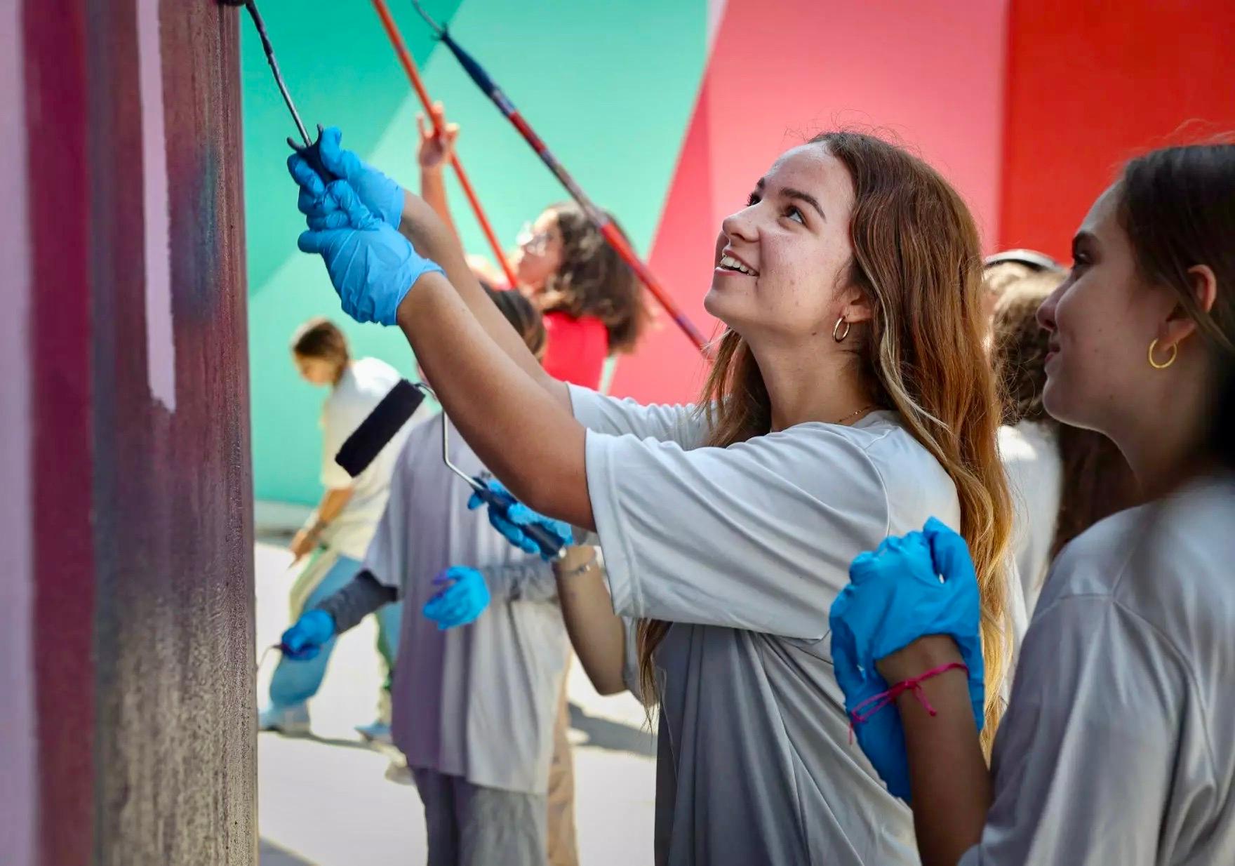 close up of two girls wearing white shirts and blue gloves looking up and painting