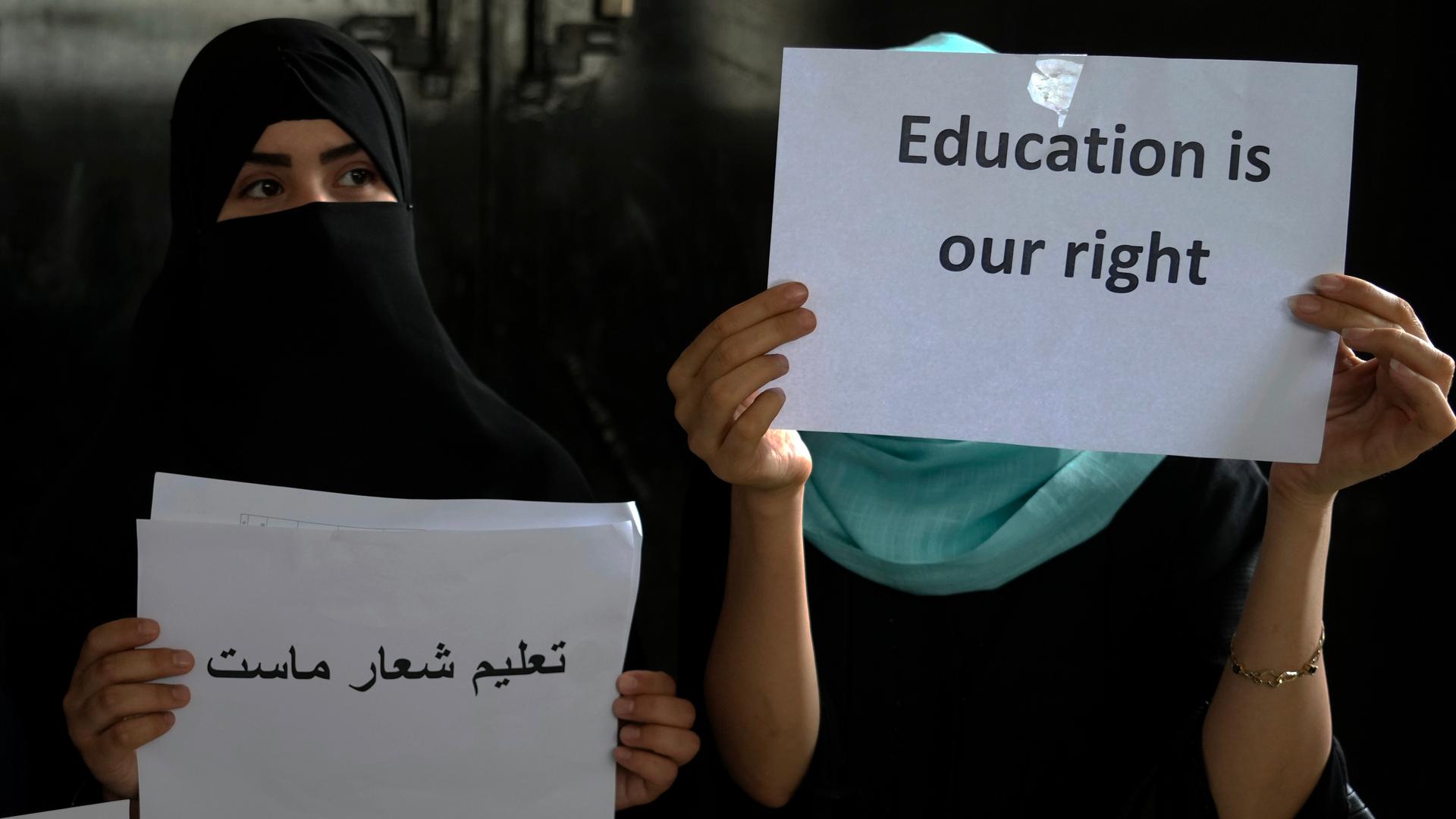 Two girls holding paper signs that say "Education is our right"