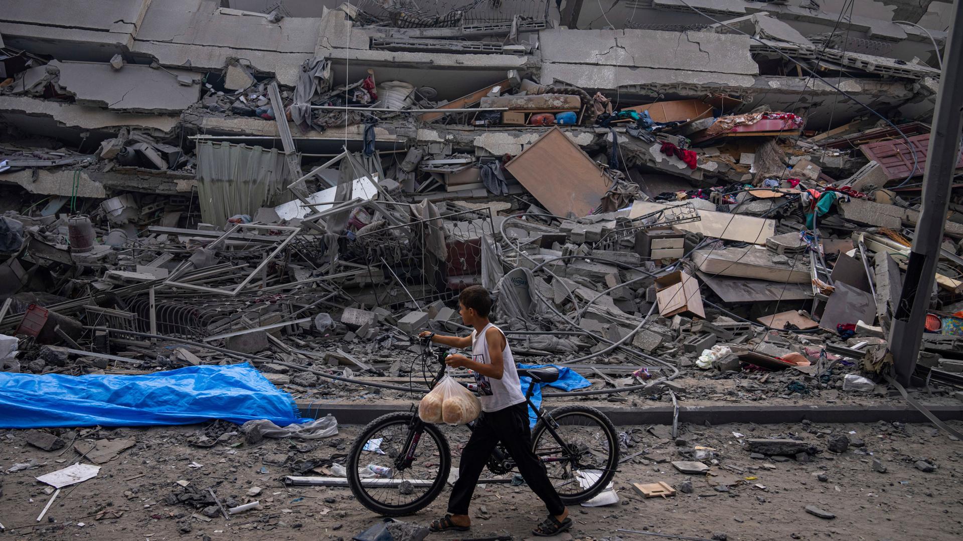 A Palestinian child walks with a bicycle by the rubble of a building after it was hit by an Israeli airstrike, in Gaza City, Sunday, Oct. 8, 2023. 
