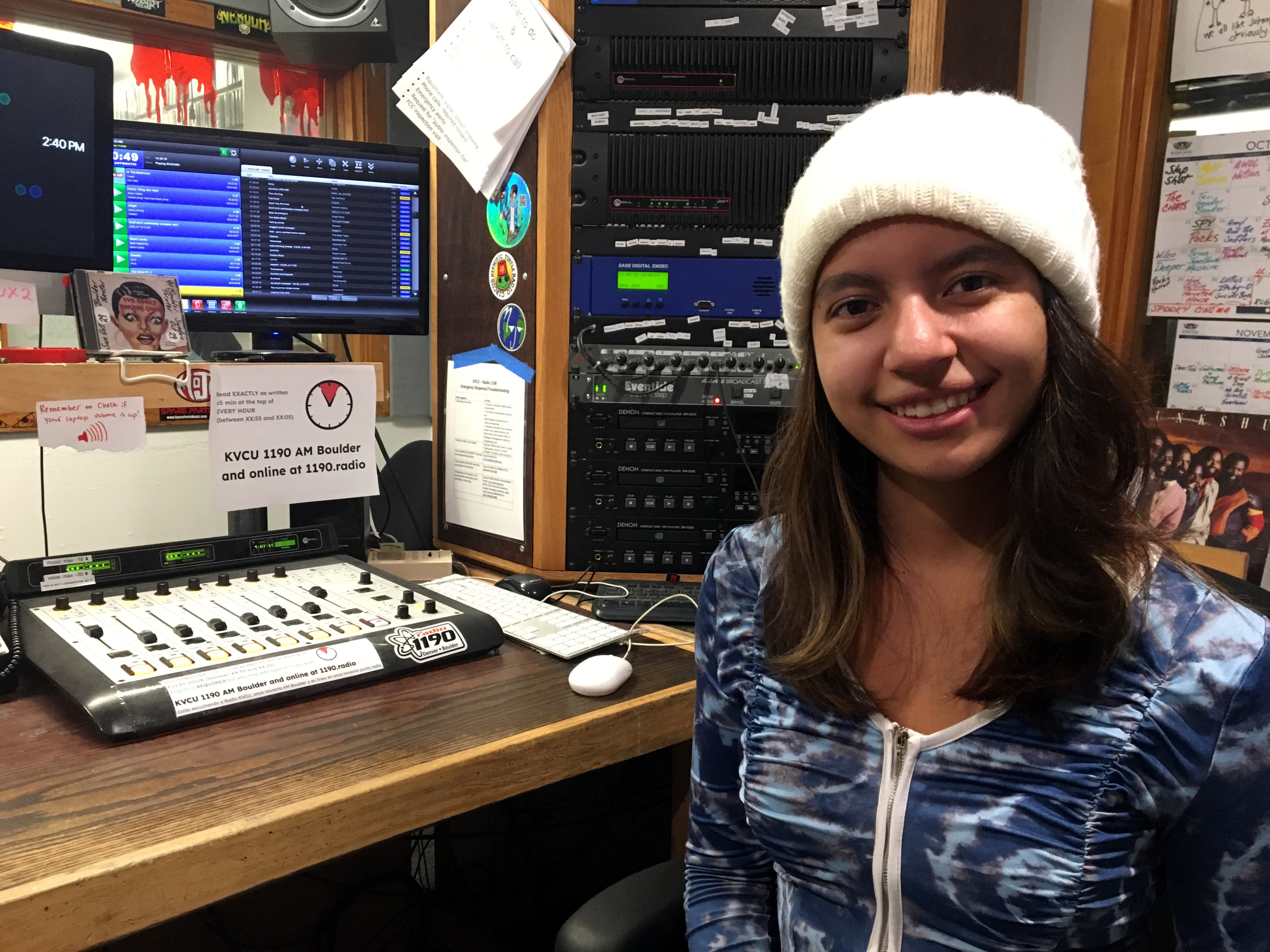 Portrait of a young woman in a studio. She is wearing a white beanie and blue zip up hoodie
