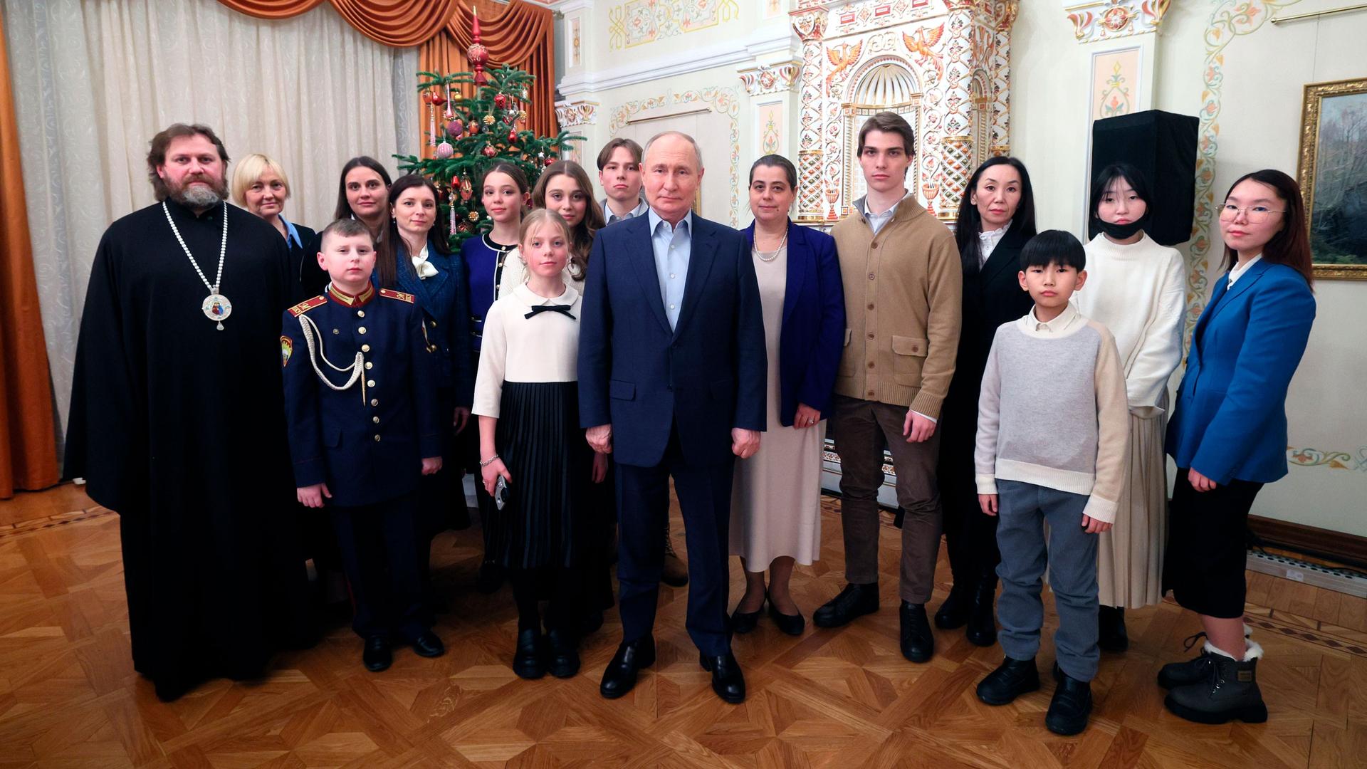 Russian President Vladimir Putin, center, and Russian Orthodox Archbishop of Odintsovo and Krasnogorsk Foma (Nikolay Mosolov), left, pose for a photo with the families of military personnel who died in combat.