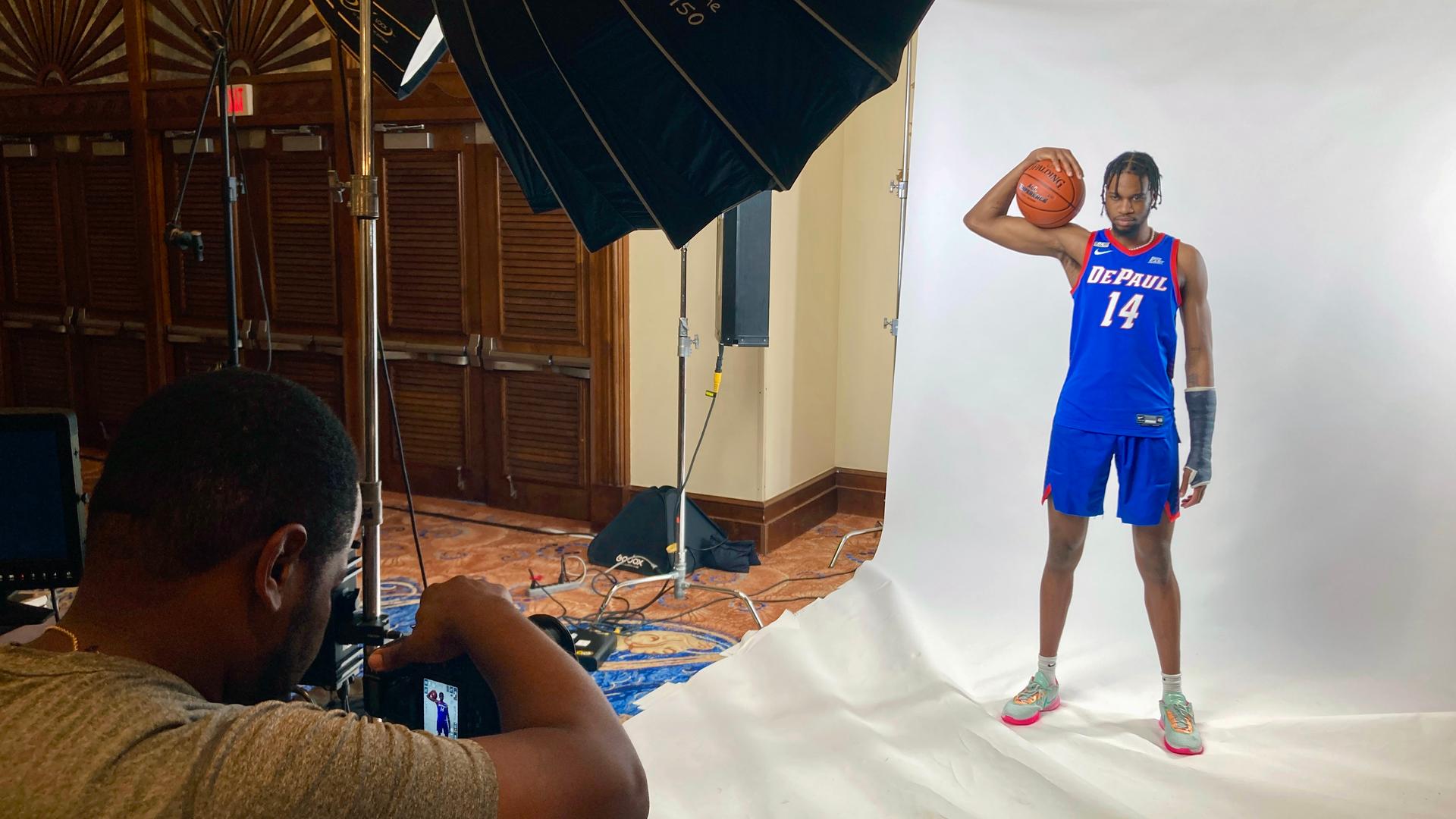 Student athlete posing in a blue uniform and holding a basketball at a photo shoot