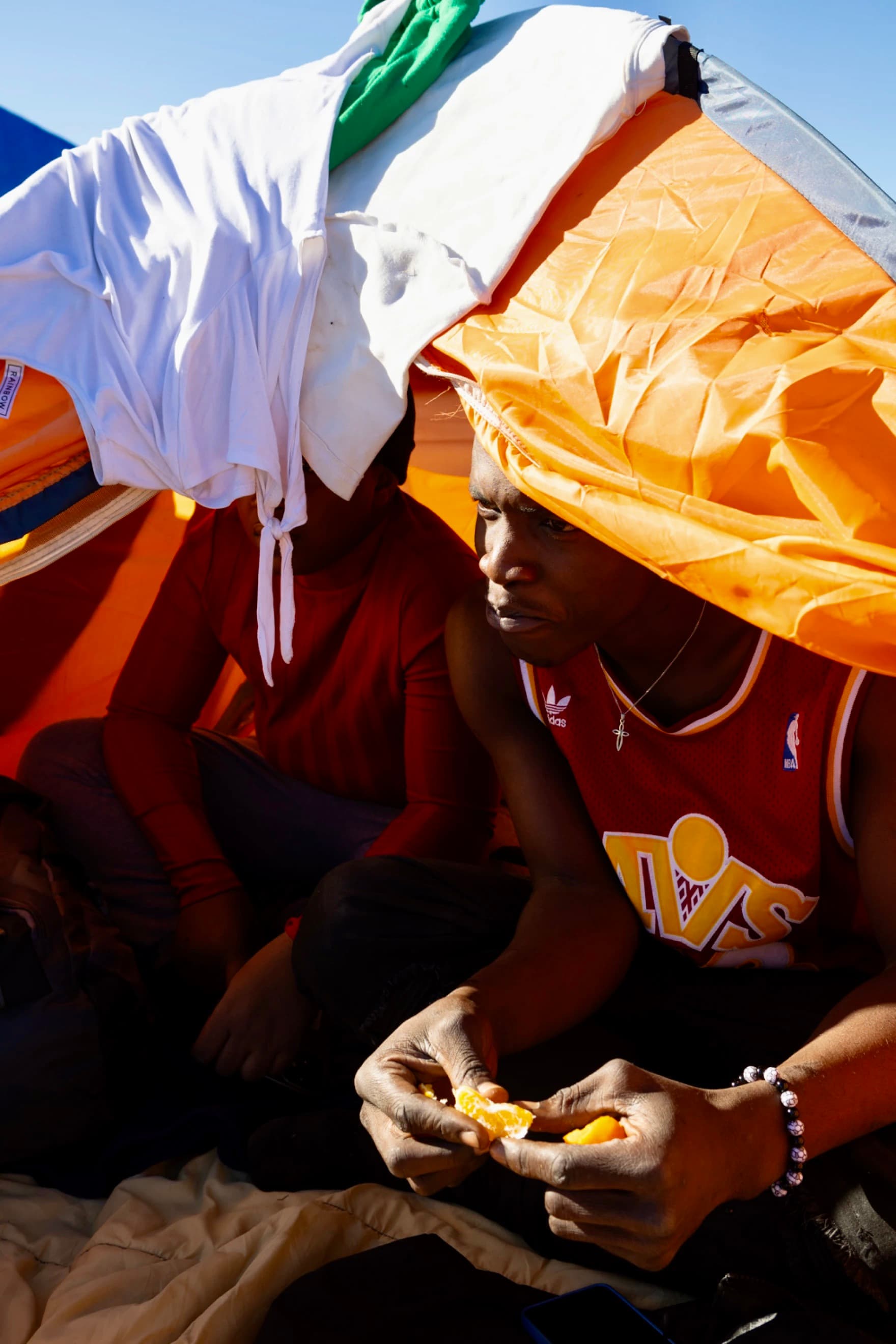A man from Cameroon eats an orange while speaking to reporters from a tent