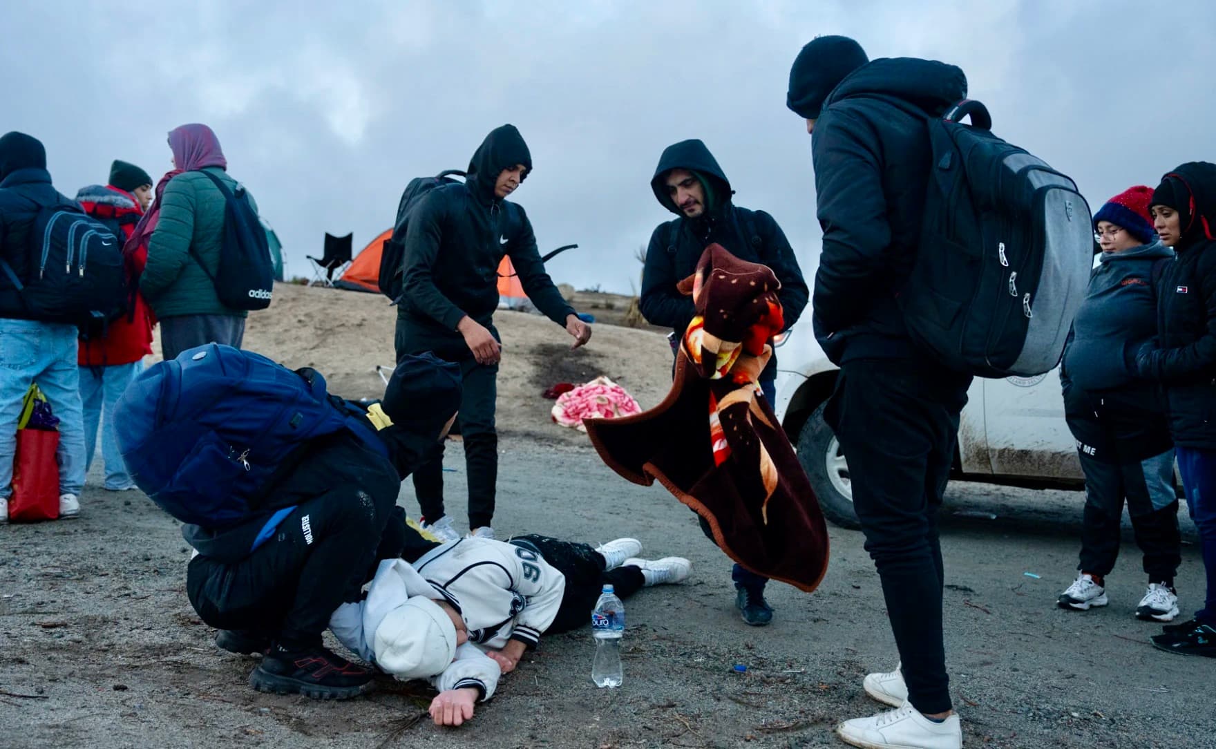 After a migrant falls sick, others help warm him and give him water