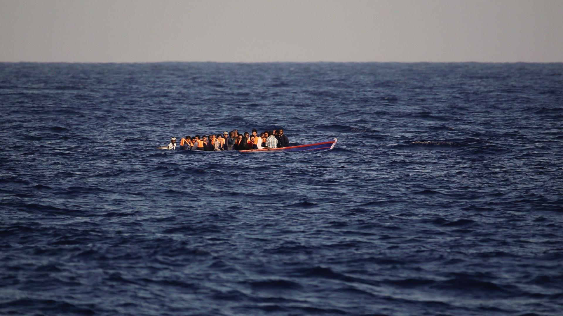 A group of people crowded onto a small open boat in the deep blue sea