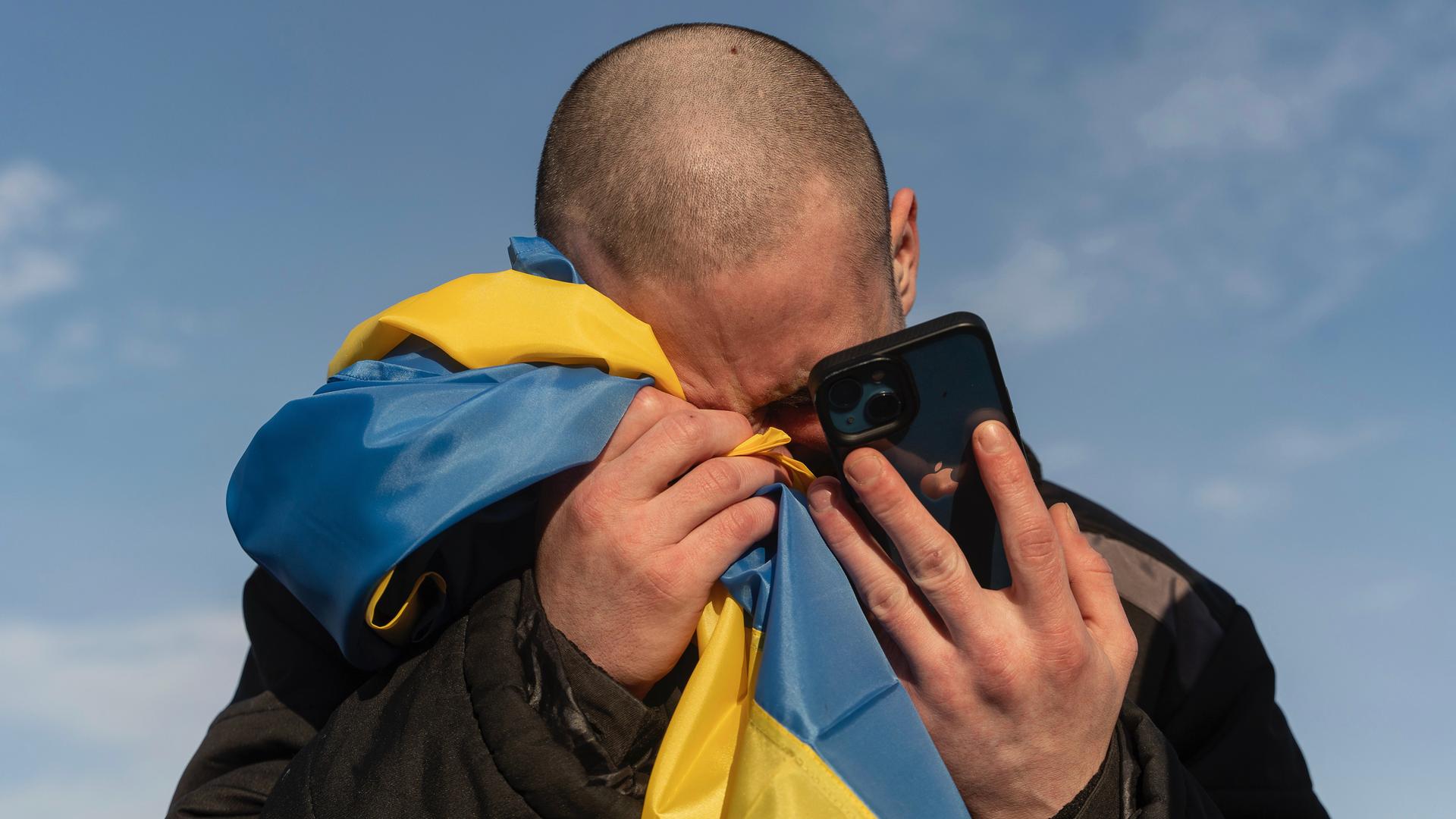 A bald-headed man buries his face in a Ukraine flag and cell phone