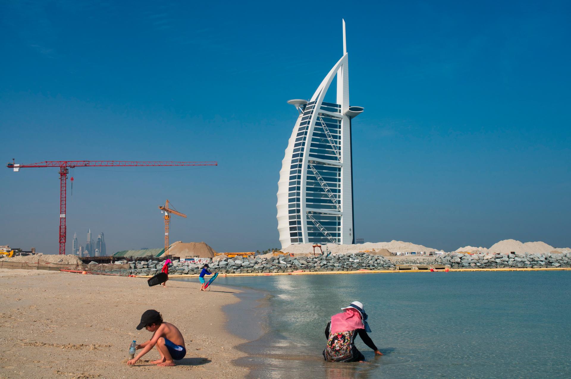 Families play on a public beach with the Burj al-Arab hotel behind them in Dubai, United Arab Emirates, Friday, May 29, 2020. 