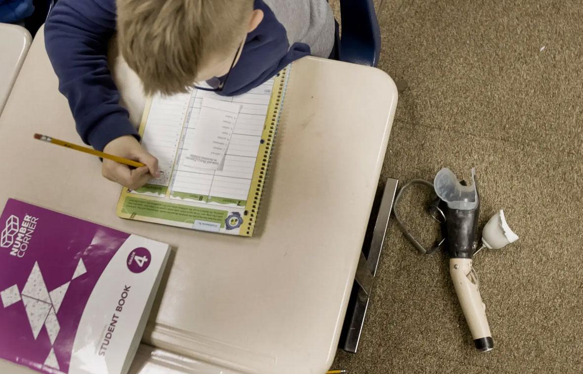With his prosthetic arm resting on the floor, Artem works in his fourth grade spelling. Artem lost his left arm after an injury from a bomb in Ukraine.