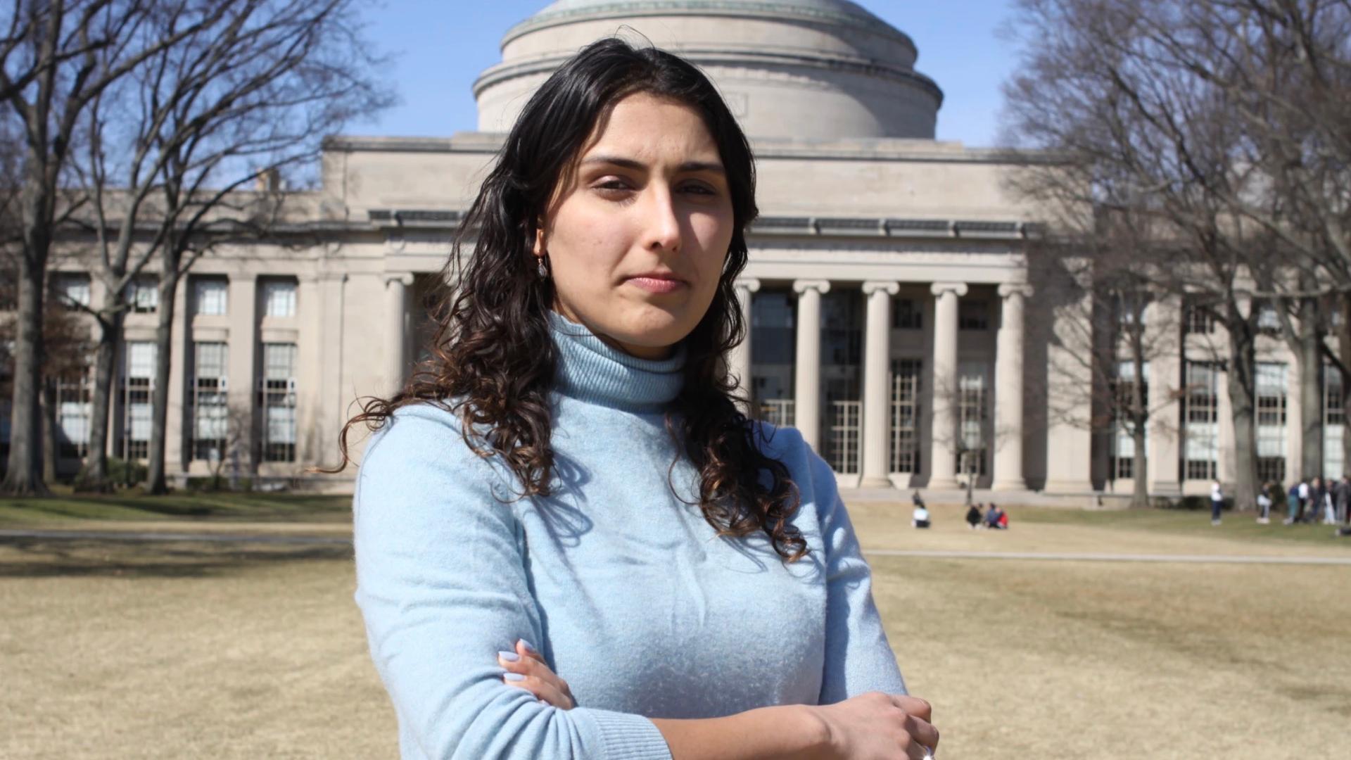 a student stands with her arms crossed in front of a domed building on MIT's campus