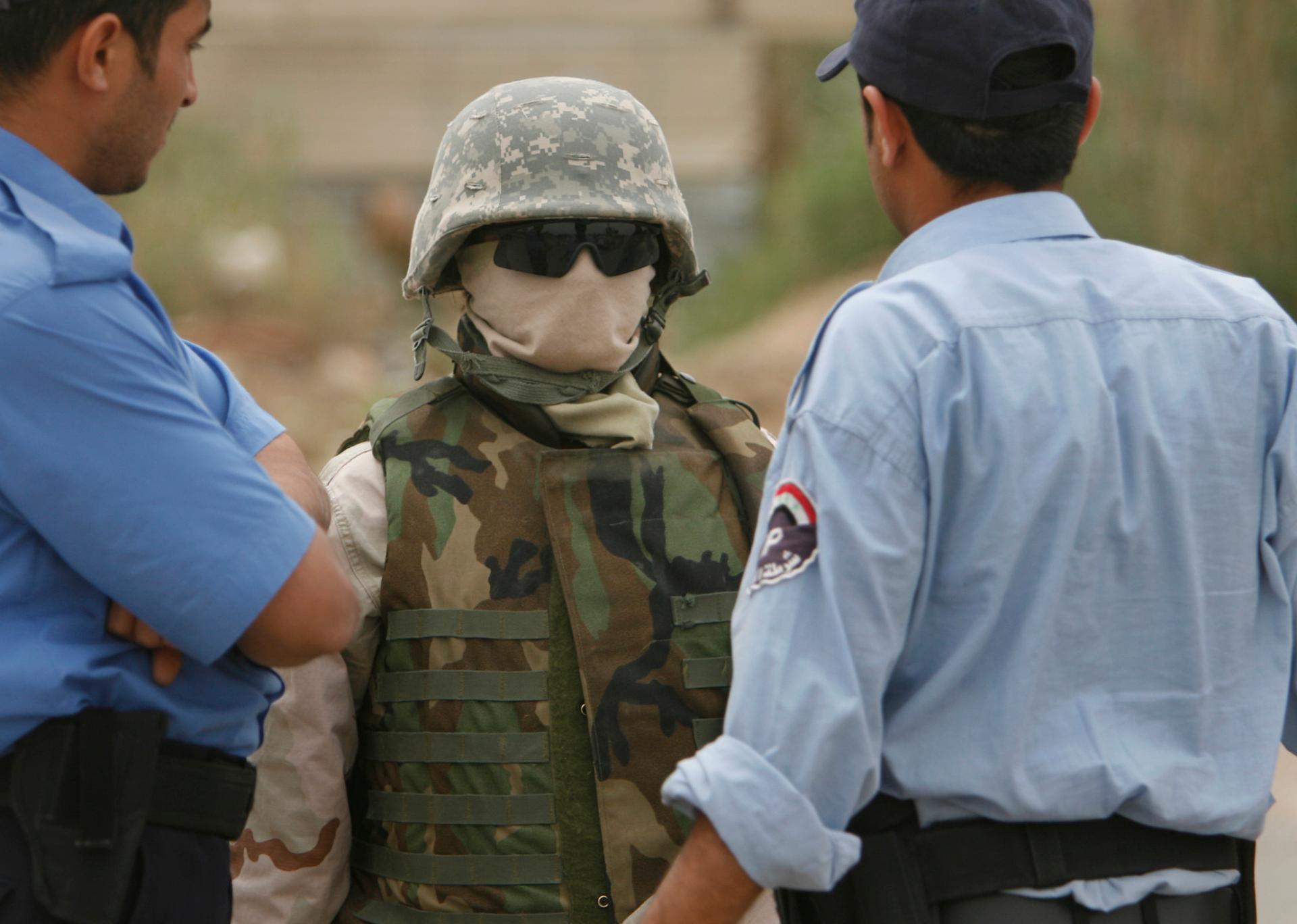 A masked interpreter talks with Iraqi policemen in Mahmudiya, south of Baghdad, April 25, 2007. Iraqi interpreters, fearing reprisal for working with US forces, sometimes wore masks to protect their identies.