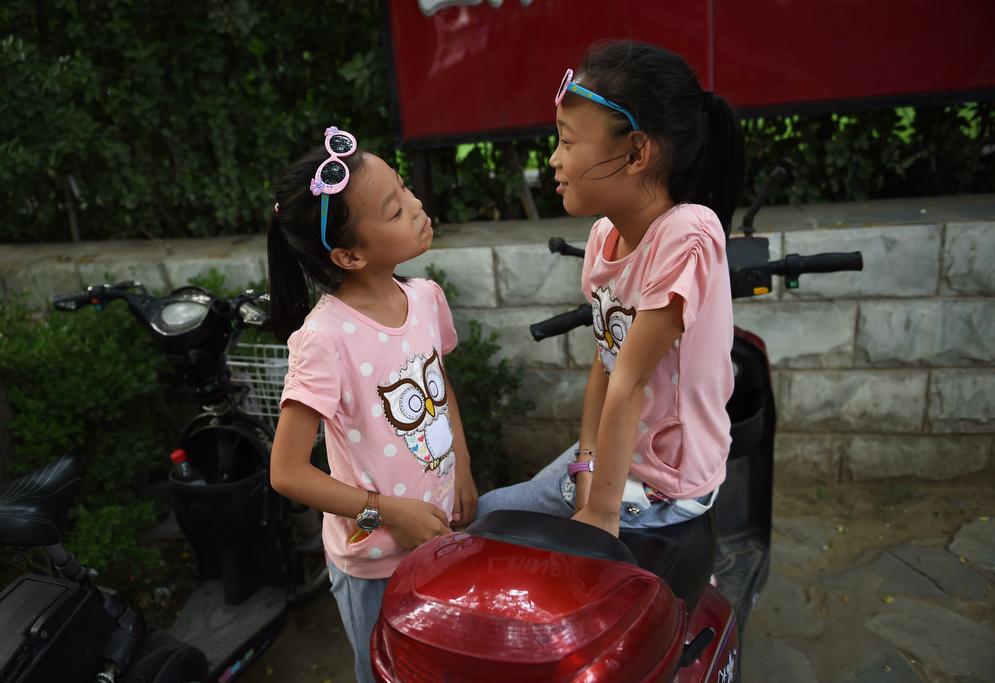 Two sisters play on their parents' electric scooter in Beijing on July 10, 2015.