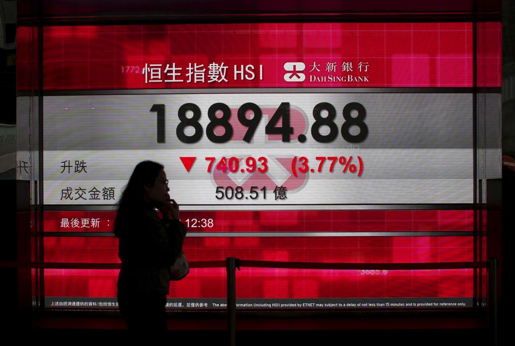 A woman talking on a cell phone walks past a panel displaying the midday Hang Seng Index in Hong Kong on Jan. 20, 2016.
