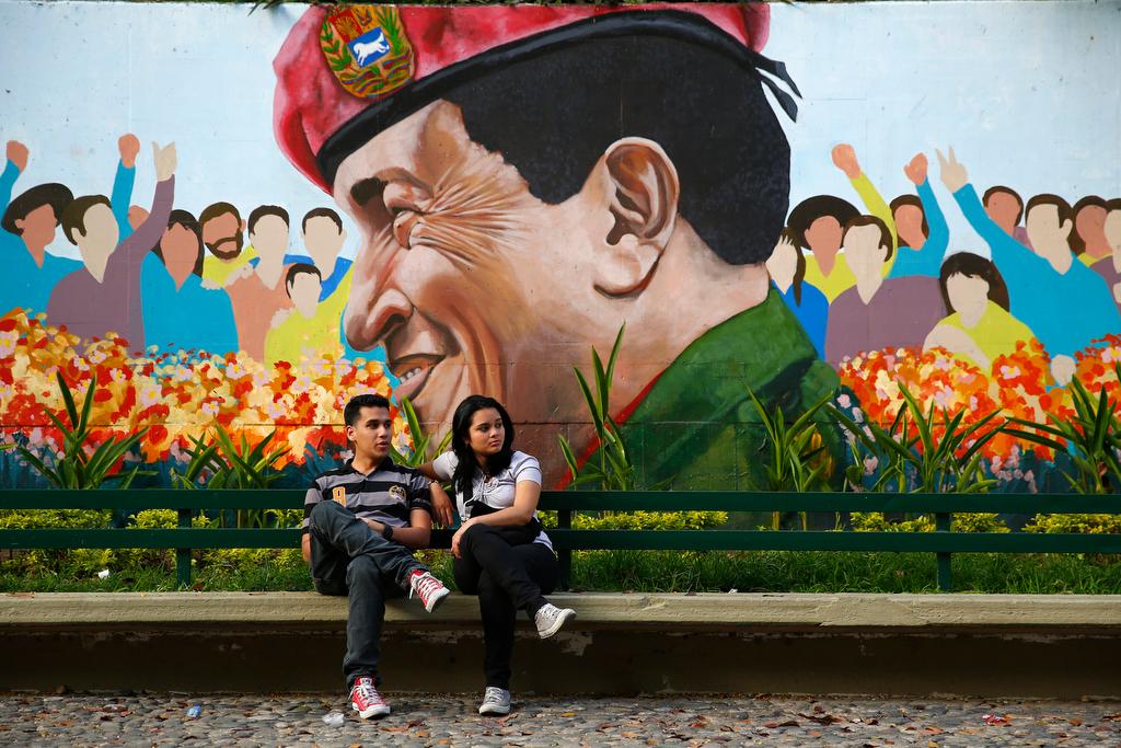 A couple sits in a park next to a mural of late Venezuela's president Hugo Chavez in Caracas on March 9, 2014.