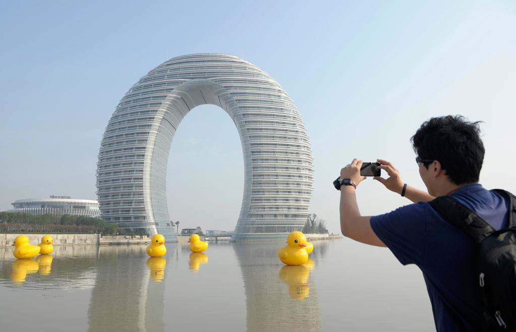 A man takes photos of the Sheraton Huzhou Hot Spring Resort, or 'Moon Hotel,' behind replicas of the rubber duck by Dutch conceptual artist Florentijn Hofman on Taihu Lake, in Huzhou, Jiangsu province, on Nov. 6, 2013.