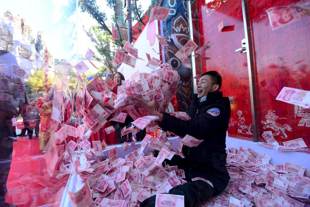 A man tries to snatch 100-yuan banknotes inside a glass cage during an event held to celebrate the upcoming Spring Festival, at a park in Hangzhou, Zhejiang province, China, on Jan. 26, 2016.