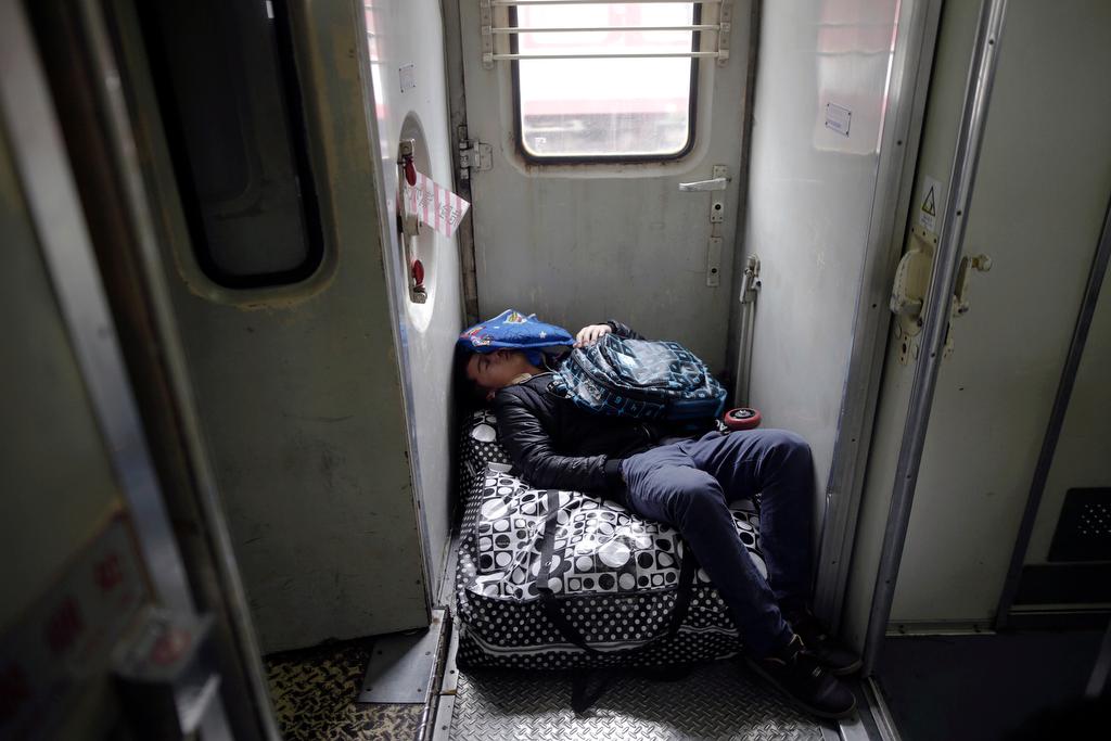 A passenger sleeps on his baggage inside a train from Shanghai to Shijiazhuang at the station in Suzhou, China, on Jan. 27, 2016, after migration for the annual Chinese Lunar New Year and Spring Festival began.