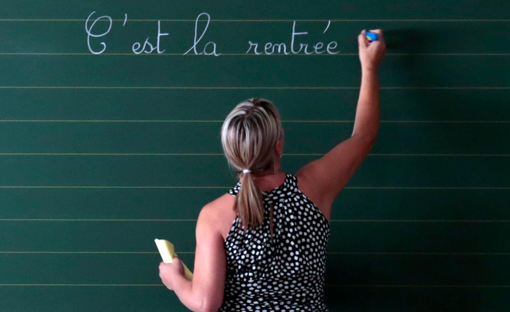 A teacher writes the phrase "Today it is the start of the new school year" on the blackboard of her classroom on the first day of the new school year at a primary school in Nice, on Sept. 3, 2013.