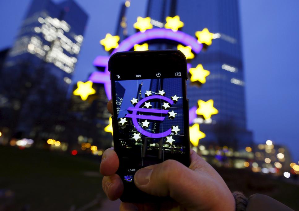 A tourist poses while taking a picture of the euro sign landmark outside the former headquarters of the European Central Bank in Frankfurt, Germany, on Jan. 19, 2016.