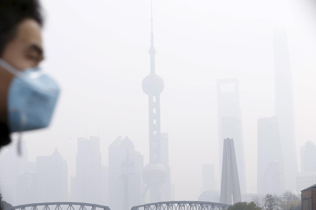 A man wearing a face mask walks across a bridge in front of Shanghai's financial district of Pudong amid heavy smog on Dec. 15, 2015.