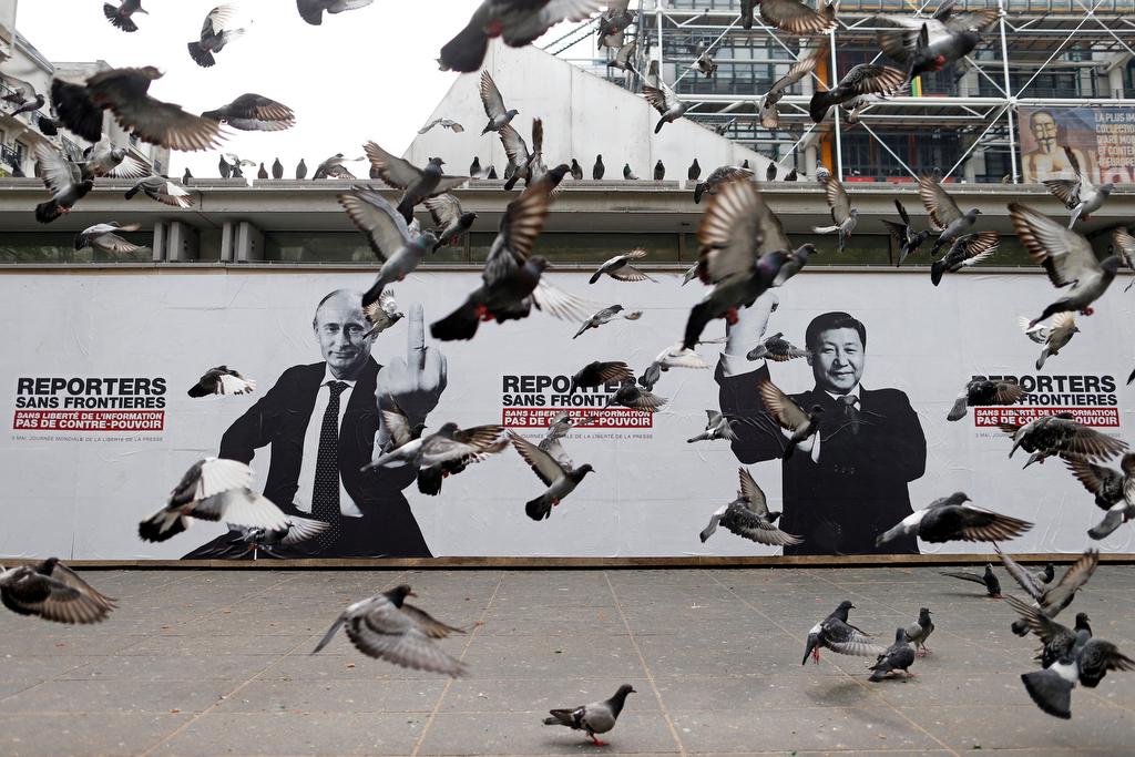 Pigeons fly past a poster depicting Russian President Vladimir Putin and his Chinese counterpart Xi Jinping (R) pasted on the Brancusi Atelier by activists from Reporters Without Borders (RSF) to mark the 20th annual World Press Freedom day in Paris on Ma