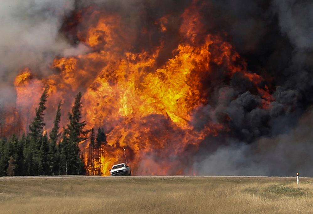 Smoke and flames from the wildfires erupt behind a car on the highway near Fort McMurray, Alberta, Canada, May 7, 2016.