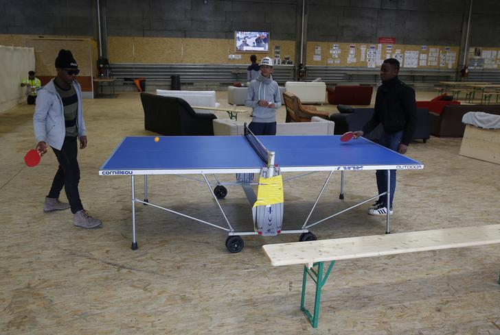 At an Army base in Thun, Zwitzerland, two young men play ping-pong at a blue table while a friend watches