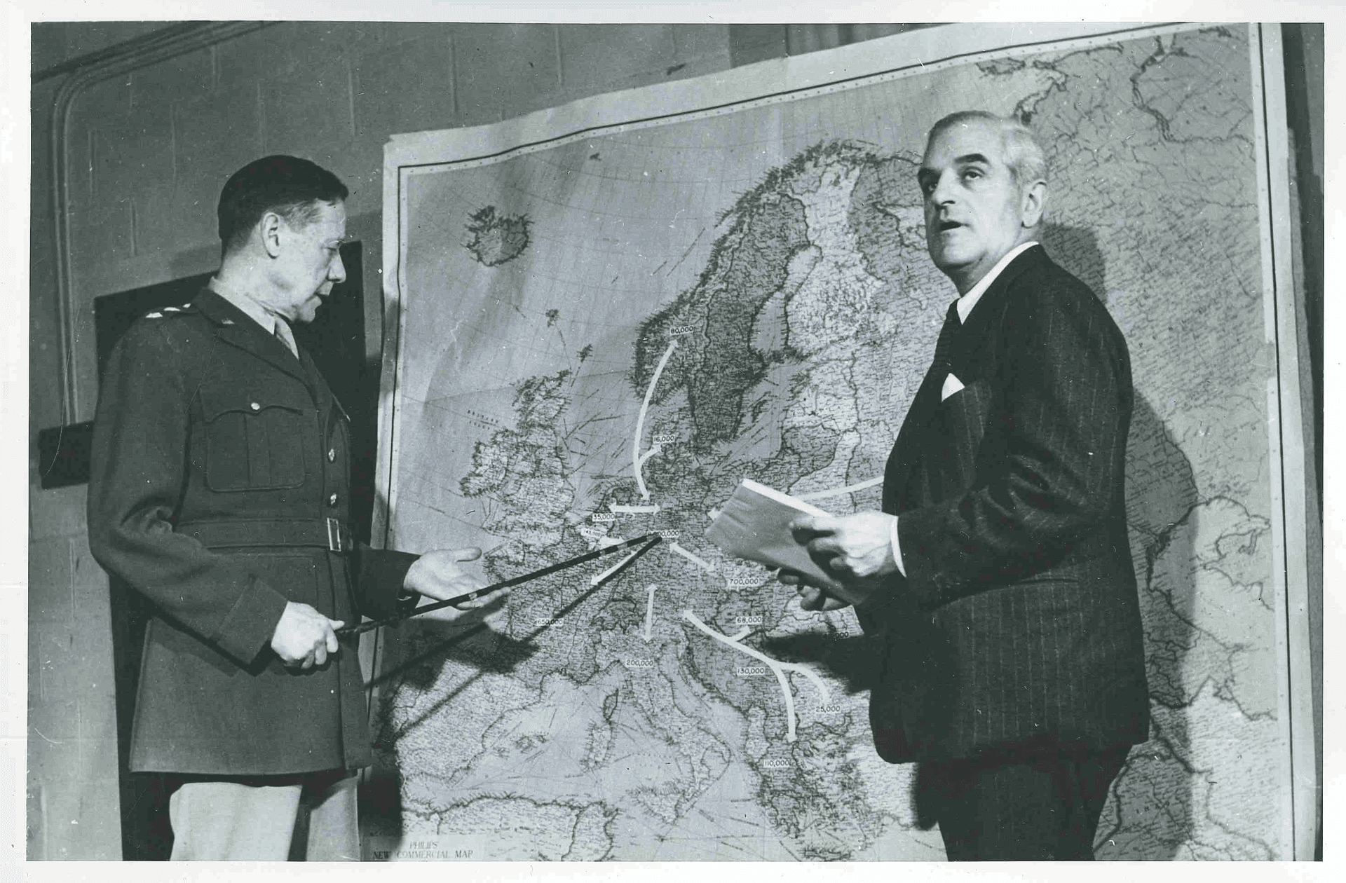 Two men point and look at a map, in black and white