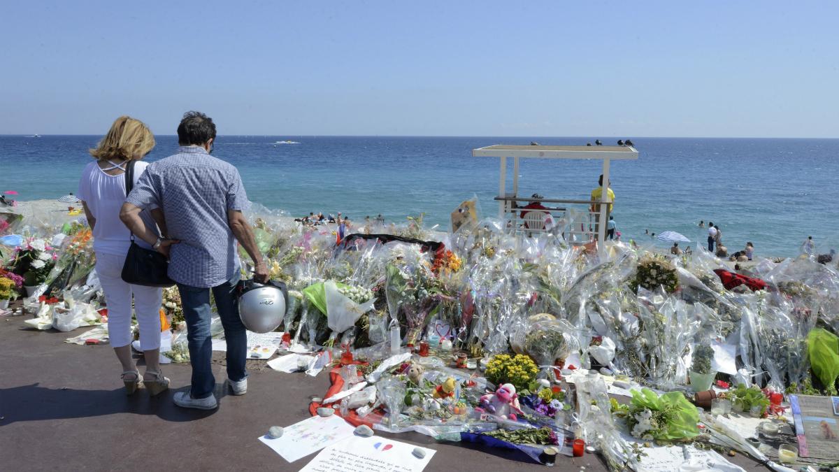 People stop near flowers left in tribute at a makeshift memorial to the victims of the Bastille Day truck attack along the Promenade des Anglais in Nice, France, July 21, 2016.