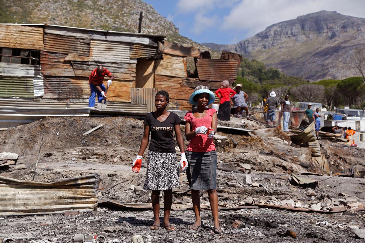 Woman stand among the remains of shacks after a fire spread through a township near Hout Bay on the outskirts of Cape Town, South Africa, December 2015.