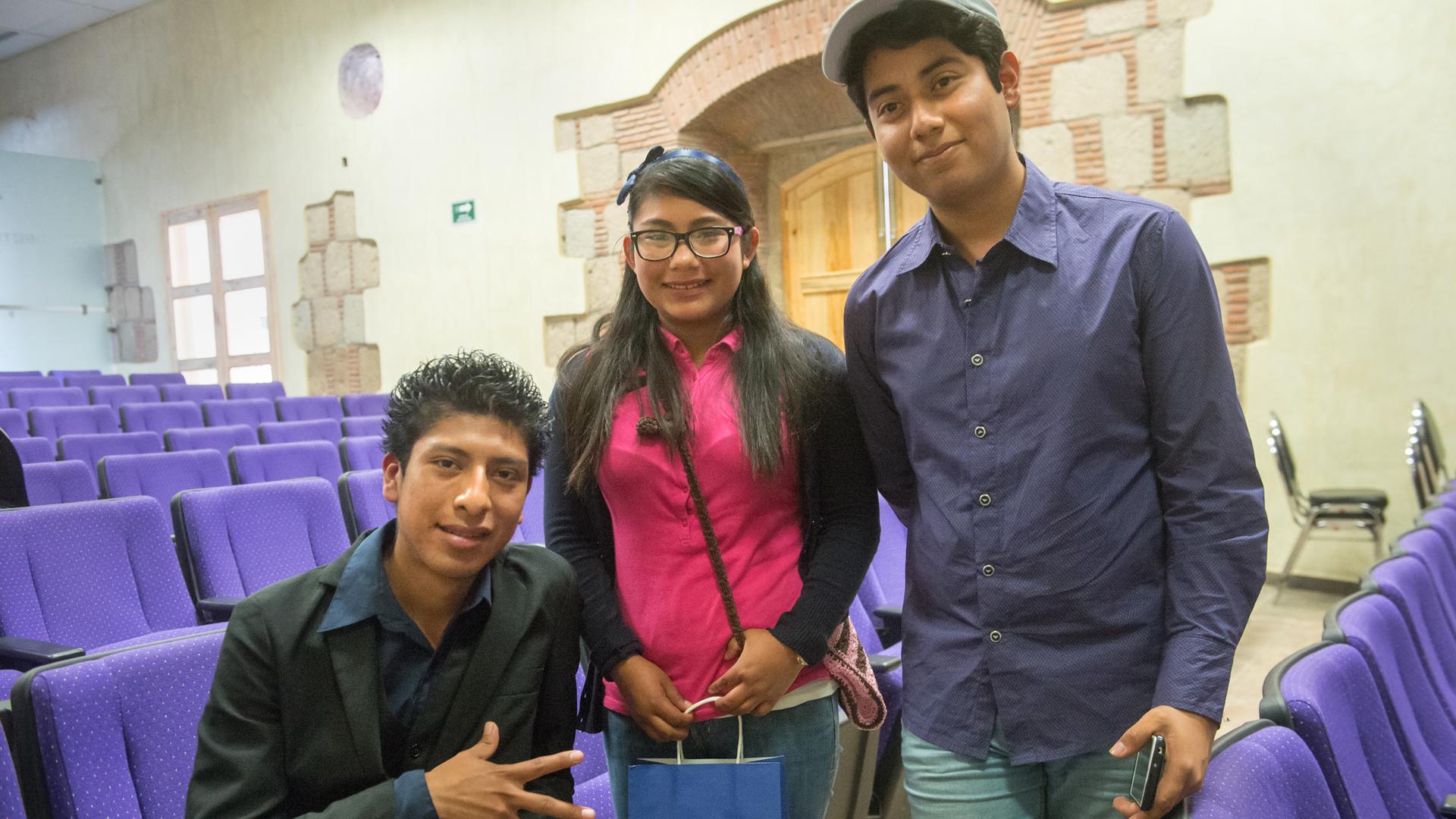 Three teens between a row of purple auditorium chairs