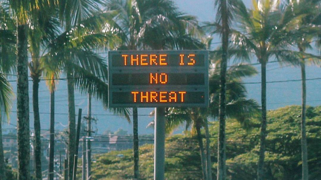 A construction sign says "There is no threat" against a backdrop of palm fronds