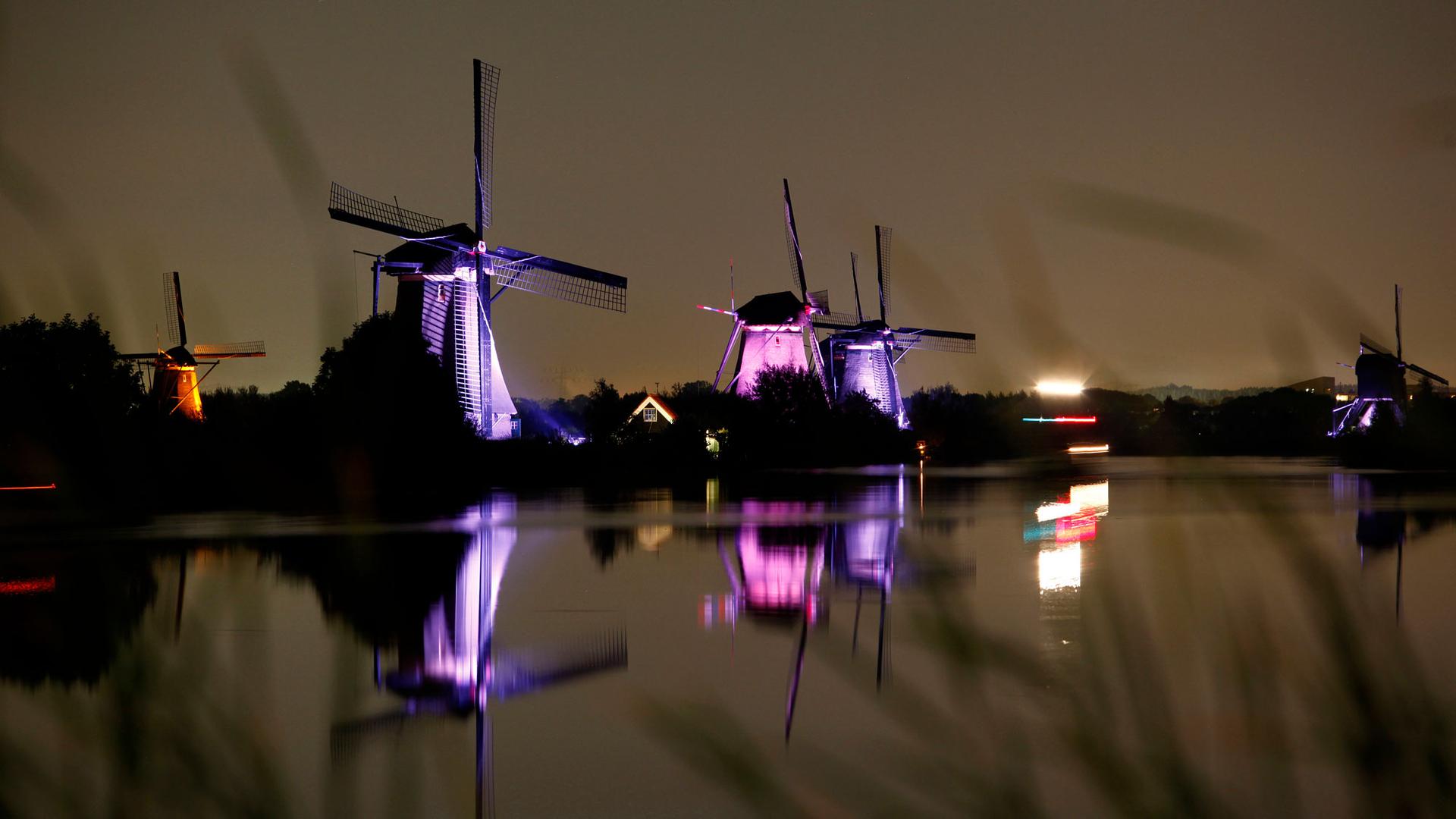 Three lighthouses line a waterway and are lit up purple and pink