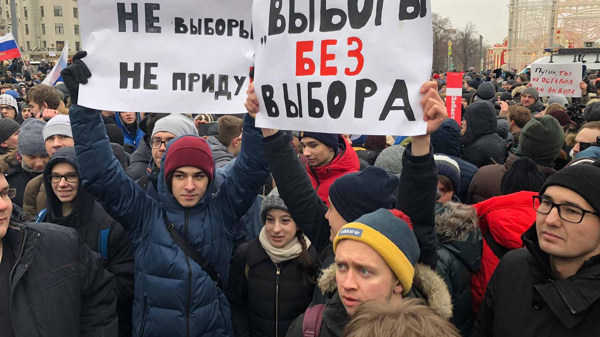 A crowd of young people are gathered. Two hold up two large signs in Russian. 