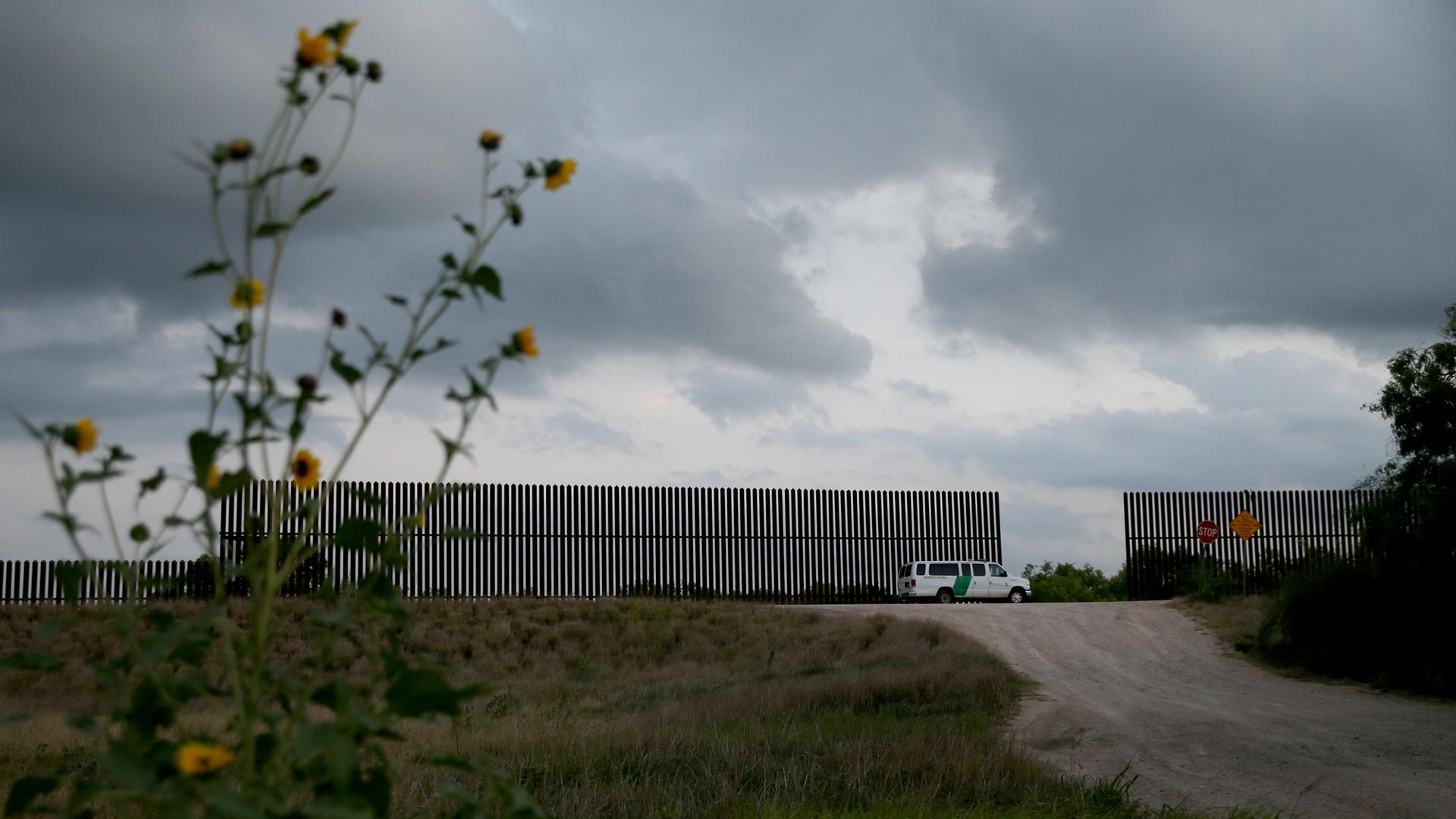 A white truck is parked between gaps in a fence against a sky of grey clouds.
