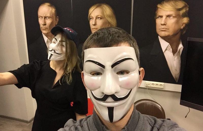 Two people in masks in front of three portraits of Putin, Le Pen and Trump